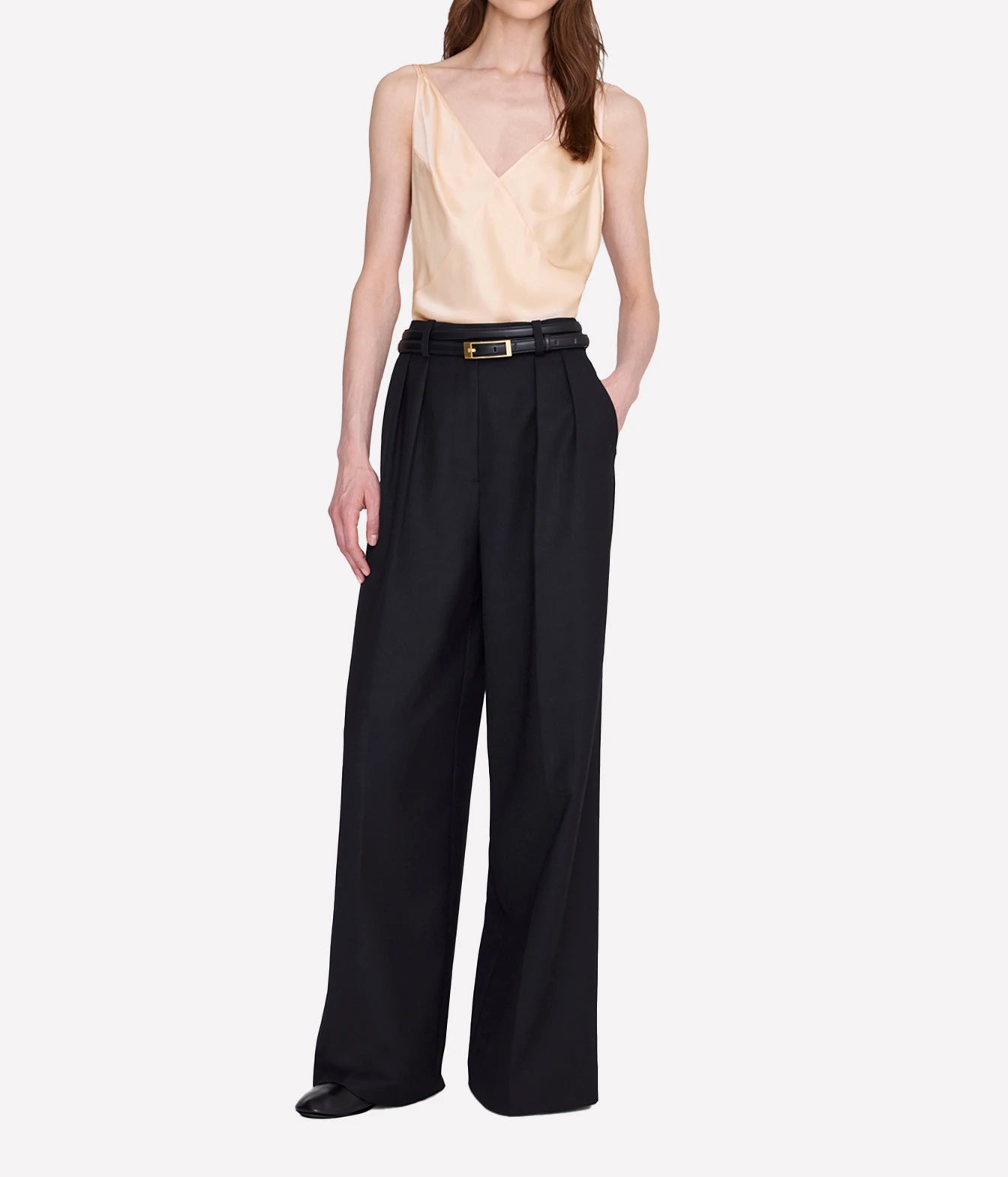 A model wearing high-waisted black wide-leg trousers with a black leather belt featuring a gold buckle, paired with a light beige satin camisole top, against a plain light gray background.