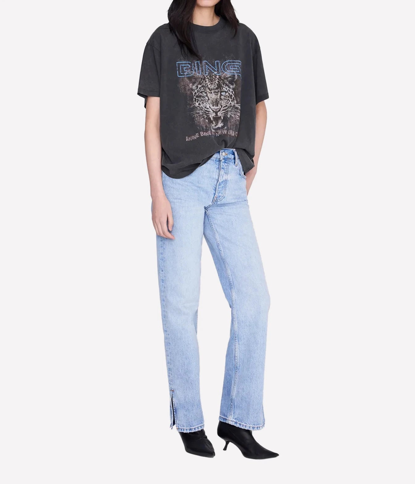 A model wearing a faded black graphic t-shirt with a leopard print and the brand name 'GINS' in blue, paired with light-wash wide-leg jeans and black pointed-toe heeled boots, set against a plain light gray background.
