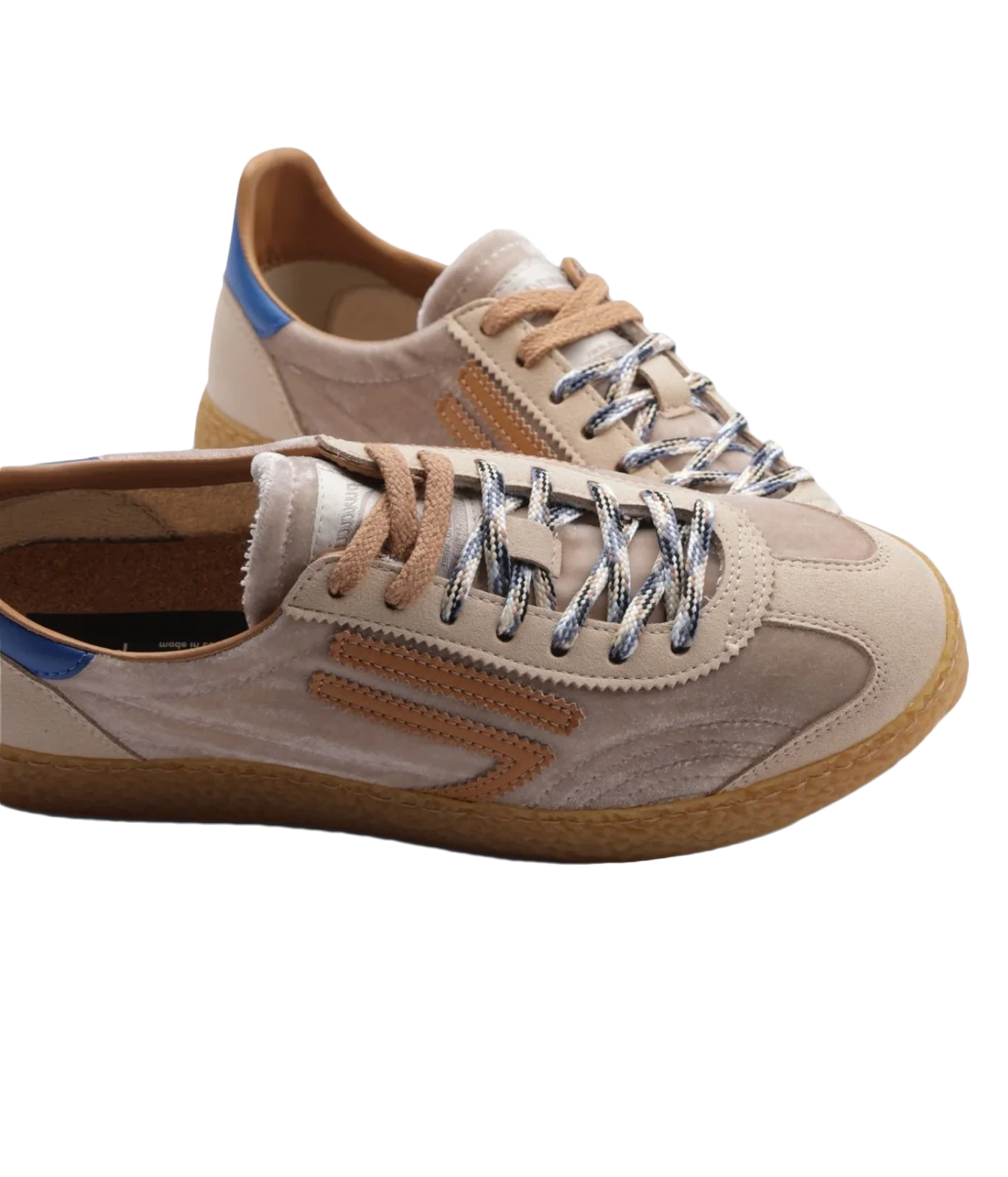 A pair of low-top sneakers in beige suede and leather, featuring metallic silver laces, a brown gum sole, and a small blue accent on the heel.