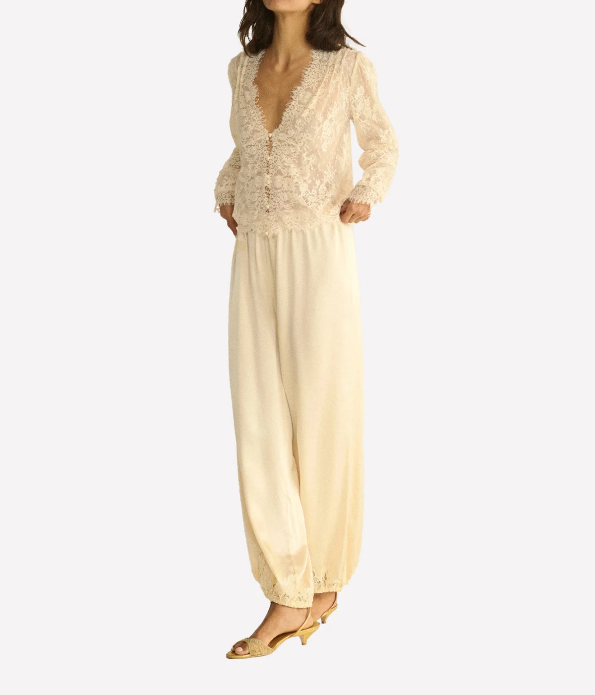 Full-length front view of a model wearing the DÔEN Amaline Top In Candlelight with cream satin wide-leg trousers gathered at the ankle and tan heeled sandals