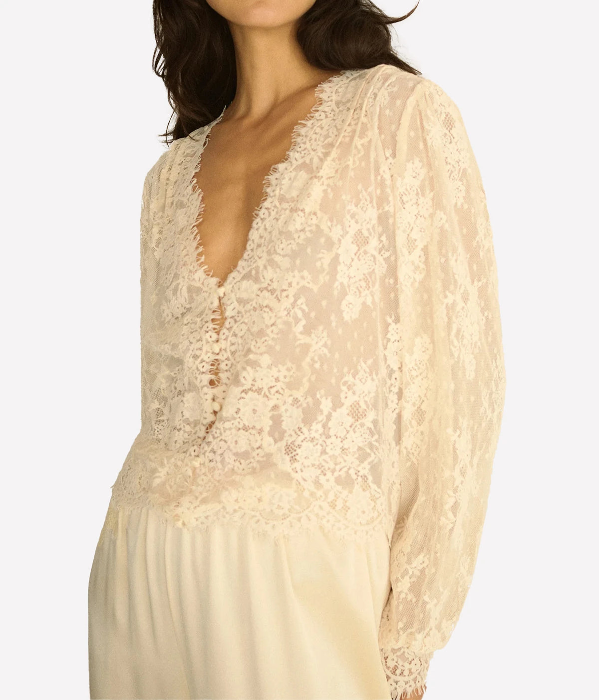 Close-up of a model wearing the DÔEN Amaline Top In Candlelight, showing the plunging scalloped lace neckline, covered buttons and balloon sleeves