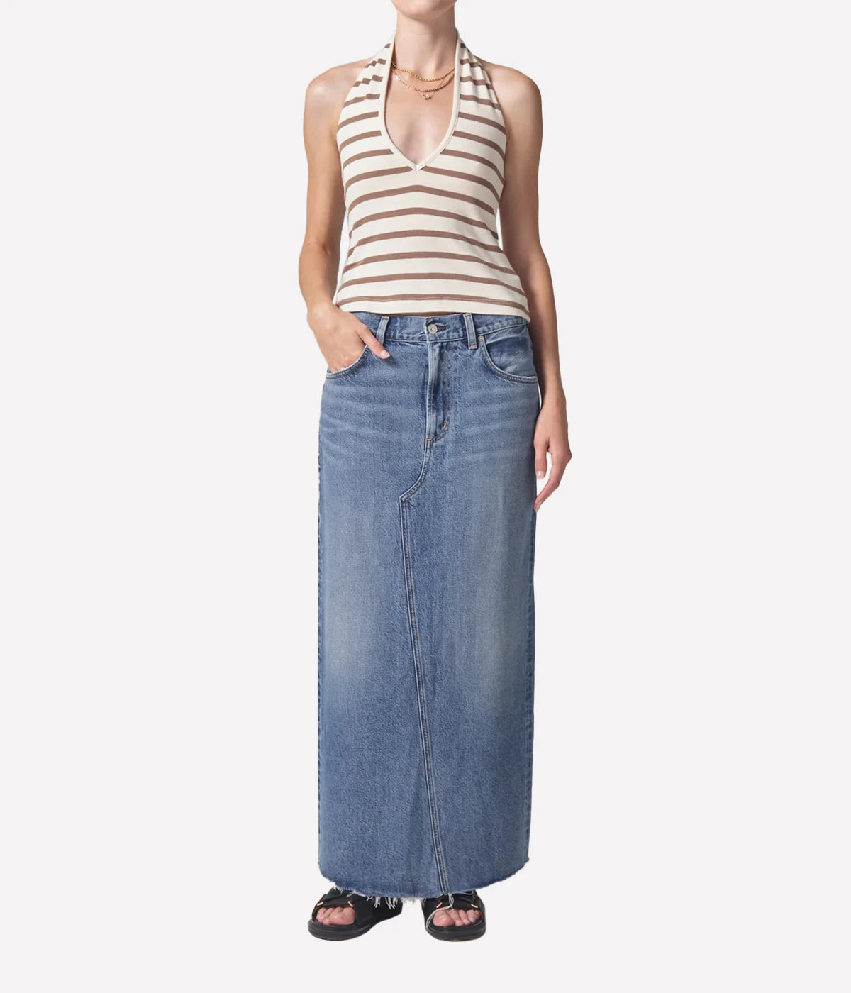 Full-length denim skirt with a raw hem and back slit detail, styled with a white tee and blazer for a modern, polished look.