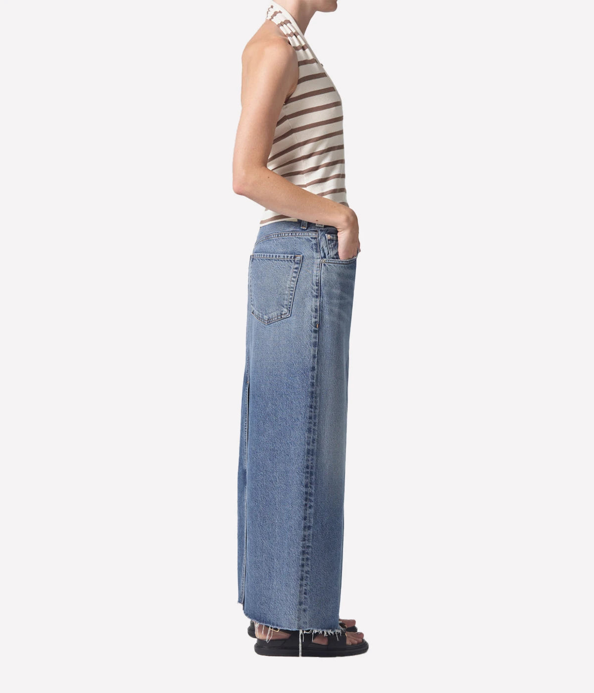 Full-length denim skirt with a raw hem and back slit detail, styled with a white tee and blazer for a modern, polished look.