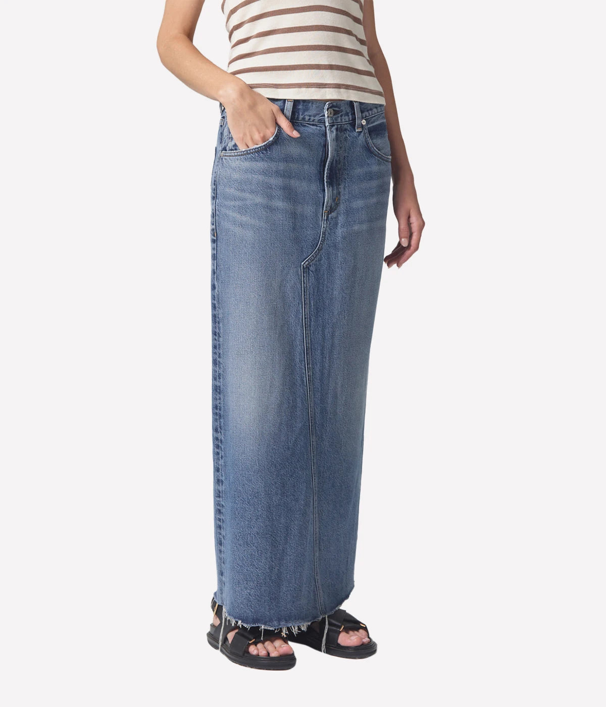 Full-length denim skirt with a raw hem and back slit detail, styled with a white tee and blazer for a modern, polished look.