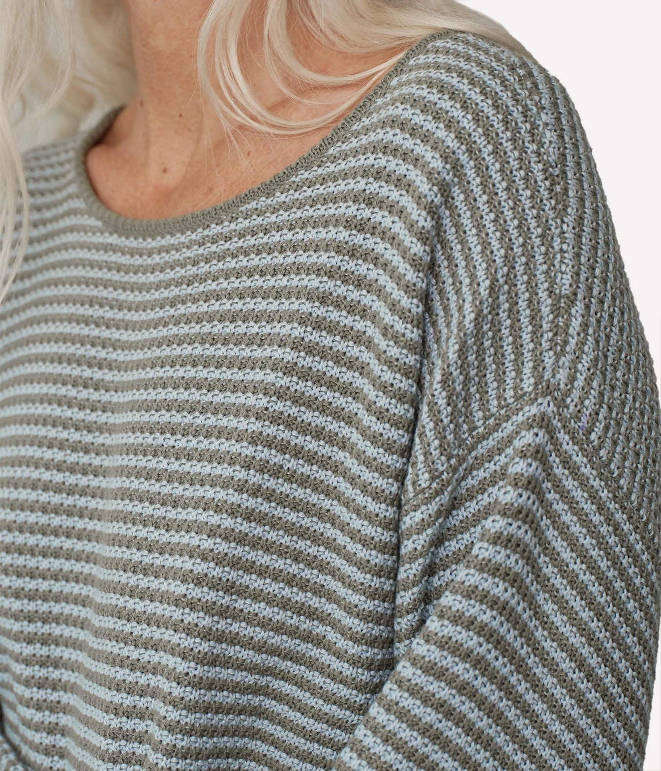 Close-up of a person wearing a textured knit sweater with horizontal gray and light blue stripes.