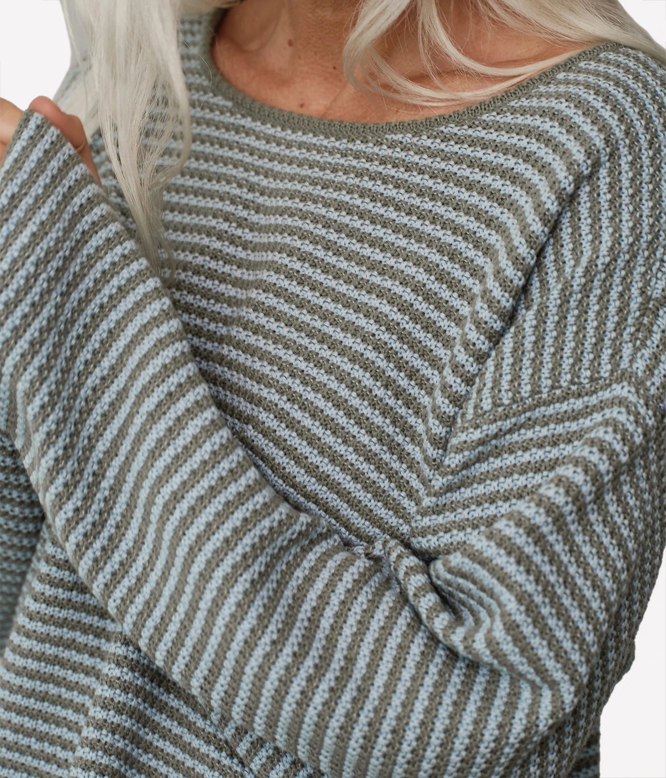 Close-up of a person wearing a knit sweater with narrow horizontal stripes in muted sage green and light gray, with blonde hair visible at the neckline.