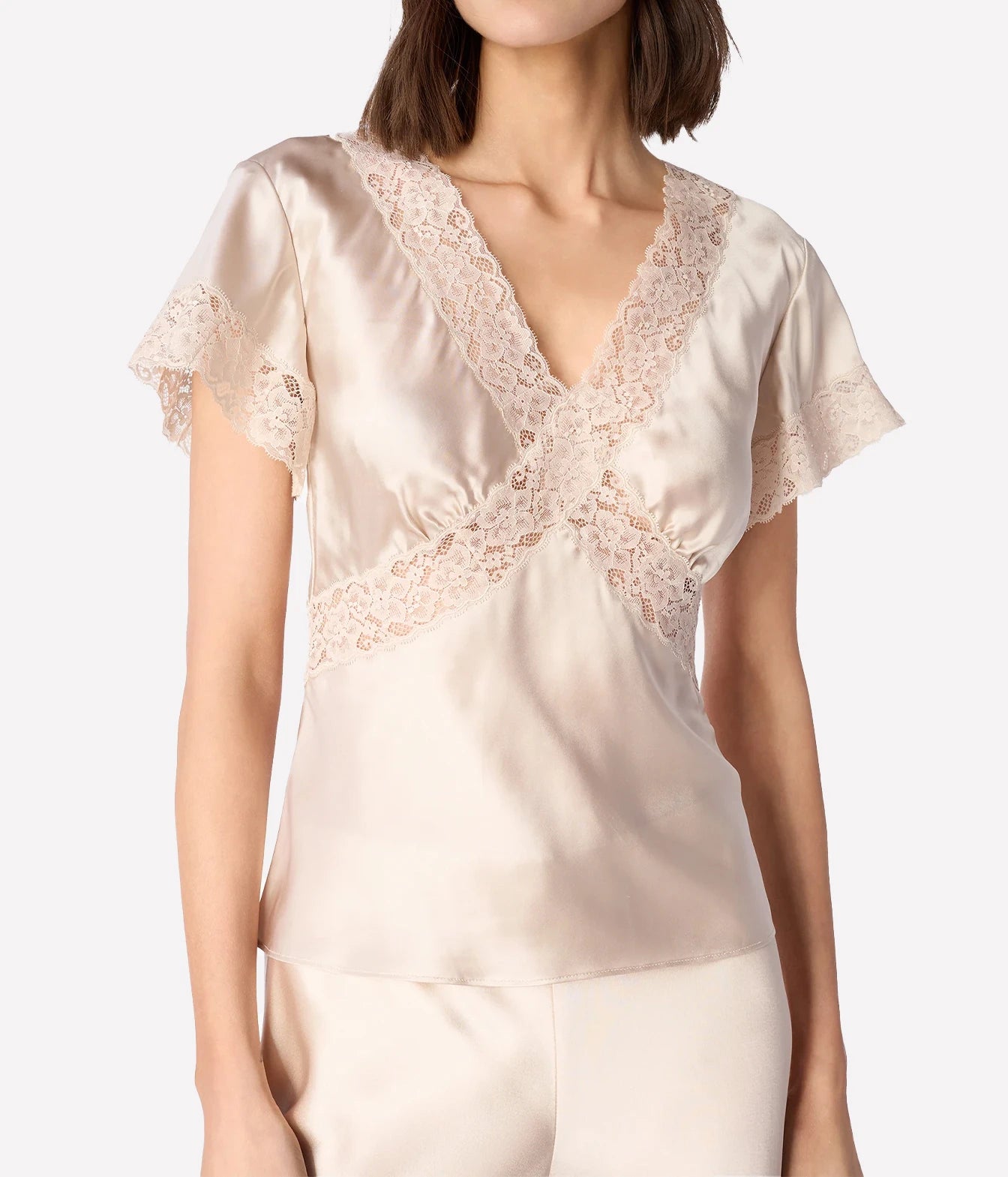 A woman wearing a champagne beige satin short-sleeve top with delicate lace trim along the V-neckline and across the chest
