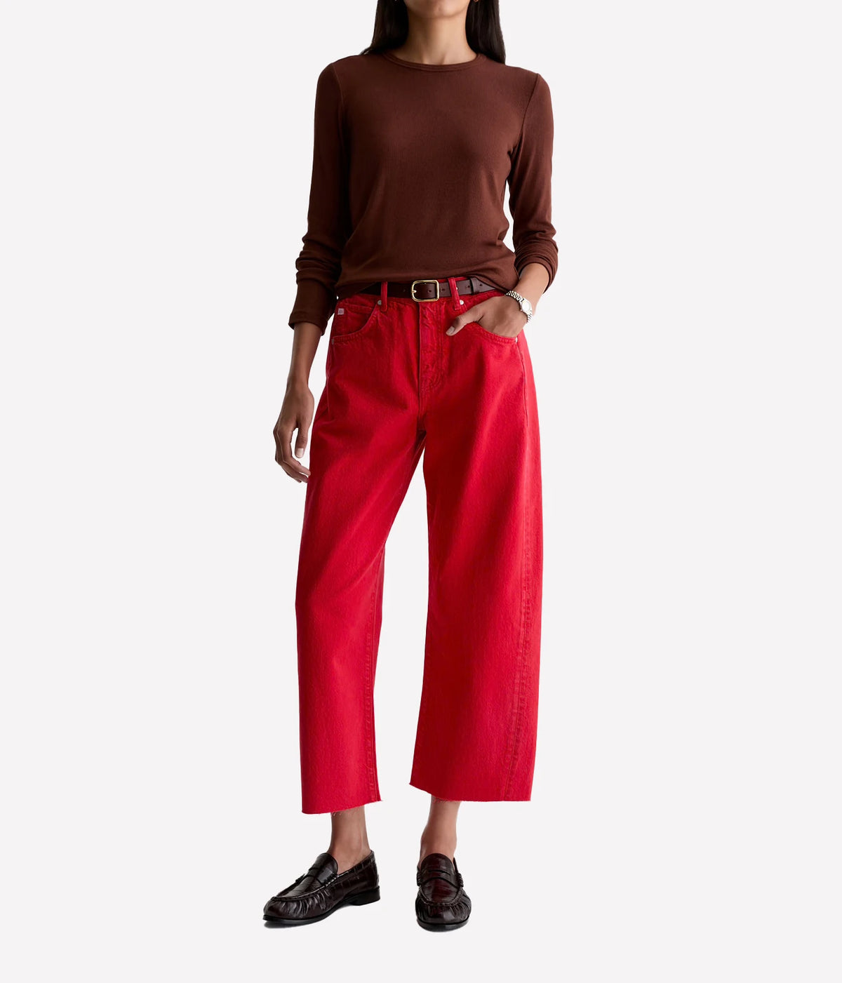 Model wearing the AG Hattie Crop in Recording Red with a fitted brown long-sleeve knit tucked in, a dark leather belt with a silver buckle, a silver watch and dark brown leather loafers