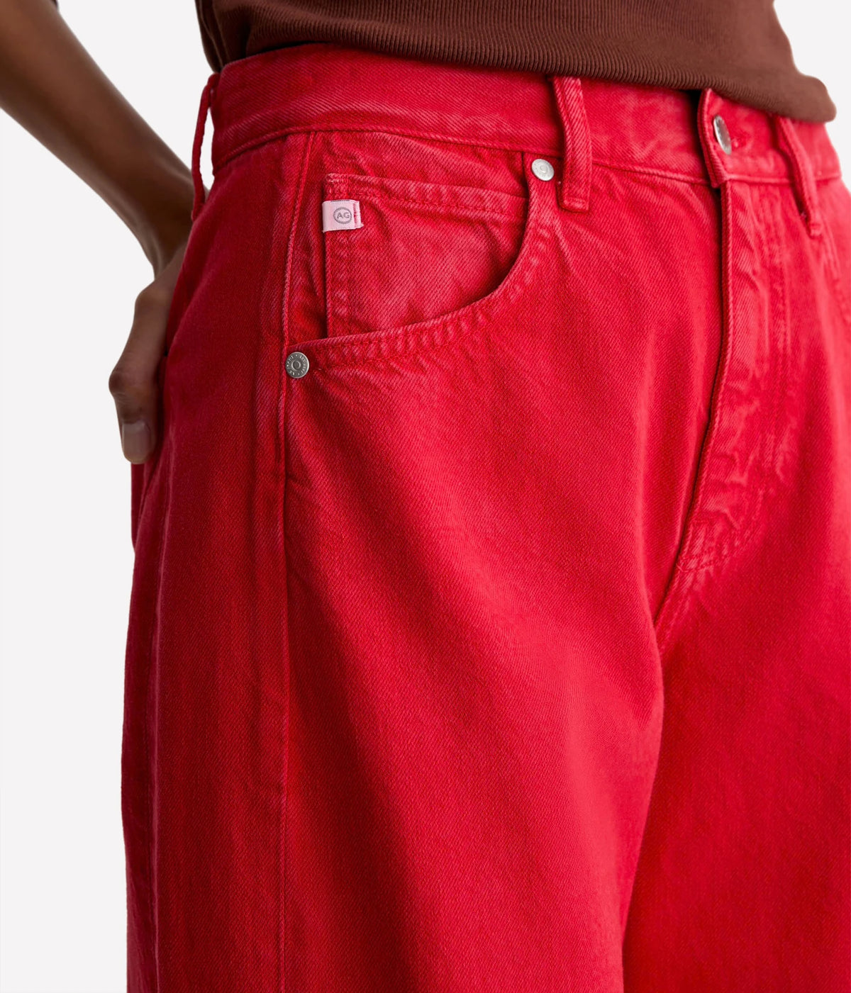 Close-up of the AG Hattie Crop in Recording Red showing the front pocket, contrast stitching, metal rivets, button fly and belt loops, worn with a brown knit top
