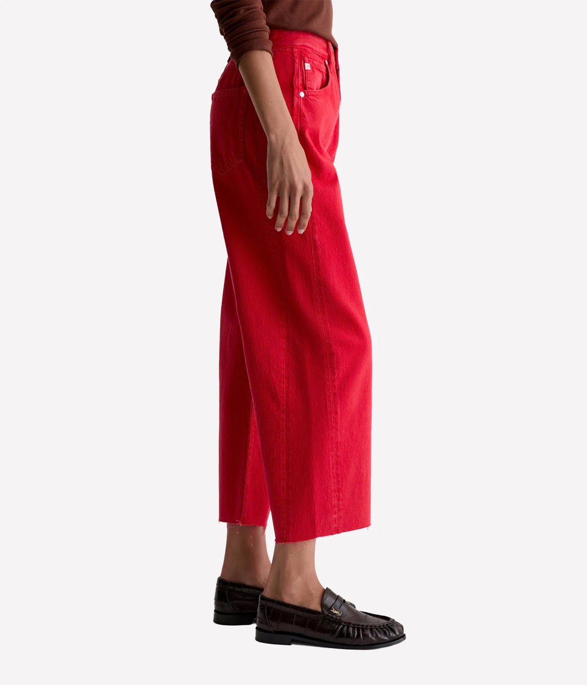 Side profile of a model wearing the AG Hattie Crop in Recording Red with a brown knit top and dark brown loafers, showing the high rise, curved side seam and ankle-grazing cropped length