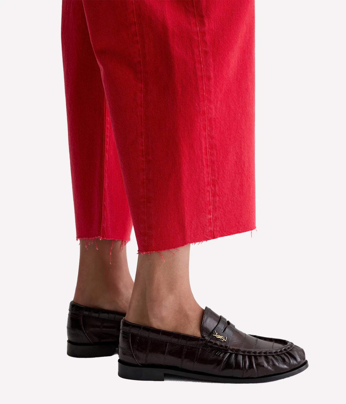 Detail of the AG Hattie Crop in Recording Red showing the raw frayed cropped hem and side seam, worn with dark brown croc-effect leather loafers