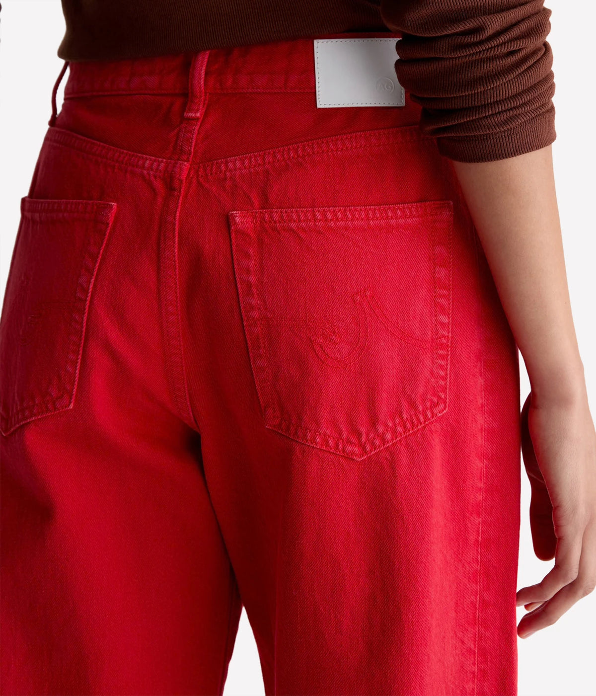 Close-up of the back of the AG Hattie Crop in Recording Red showing the stitched back pocket detail, yoke seam and white waistband patch, worn with a brown knit top