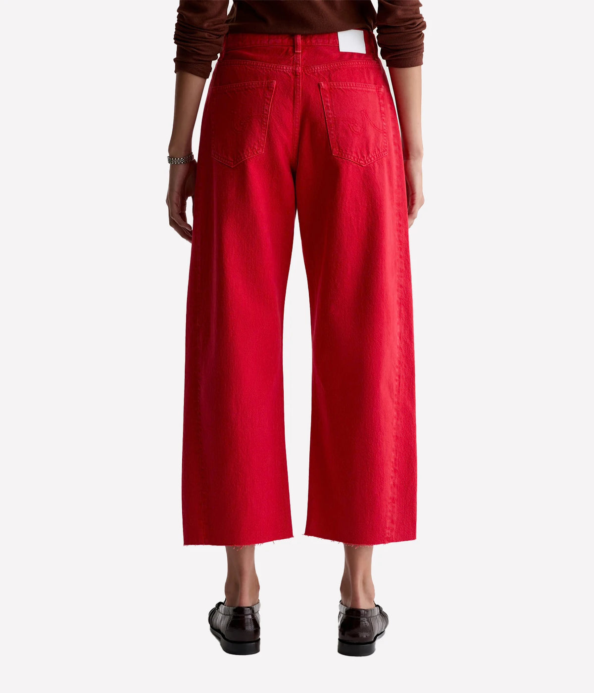 Back view of a model wearing the AG Hattie Crop in Recording Red with a brown knit top and dark brown loafers, showing the back patch pockets, white waistband patch and wide cropped legs