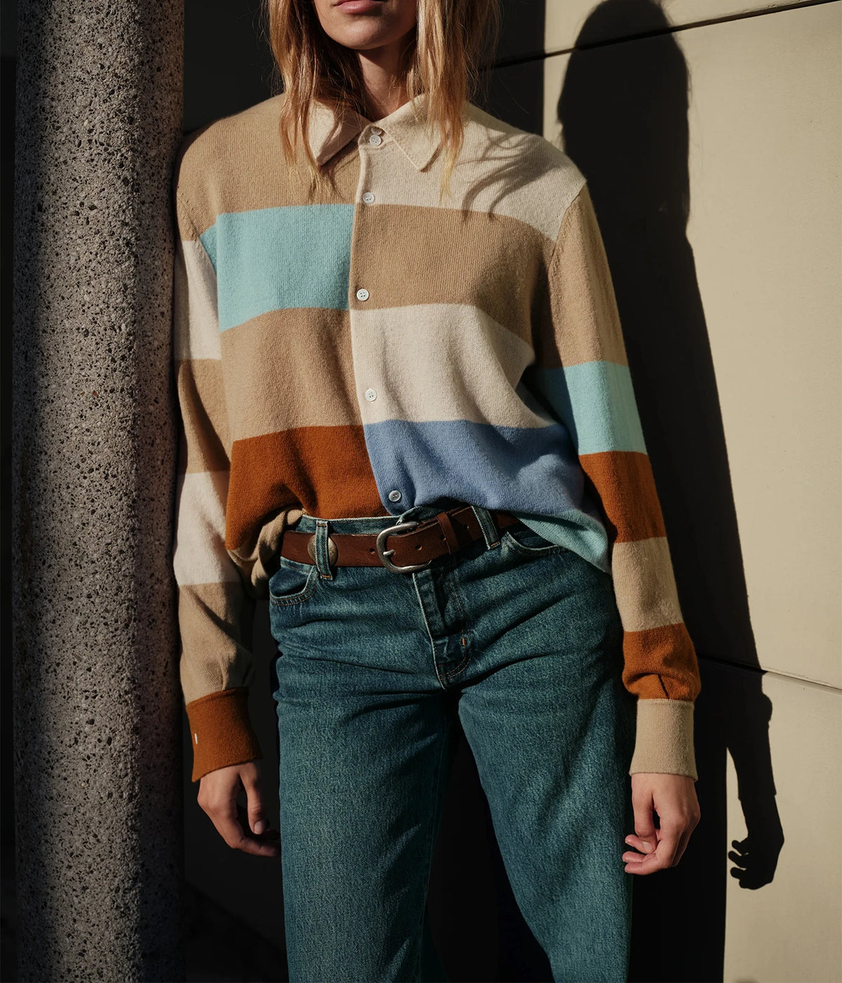 Model wearing the CISSA Rugby Cardigan in Desert Sky tucked into dark teal jeans with a black western belt and silver buckle