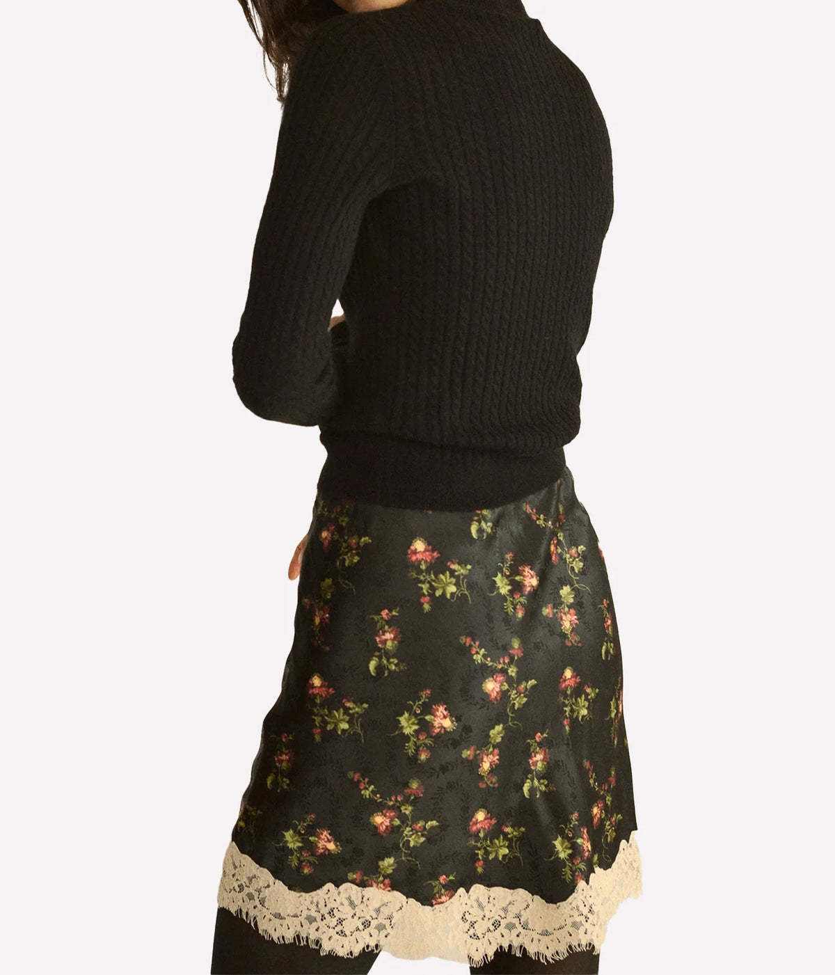 Back three-quarter view of a model wearing the DÔEN Giulietta Skirt In Noir Hillside Thistles with a black ribbed knit, showing the lace hem
