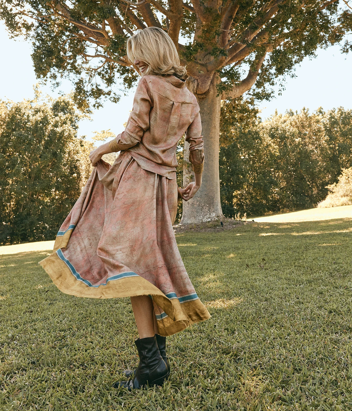 Pierre-Louis Mascia Aloe Silk Skirt in Terracotta Multi, back view on model with the matching Aloe Shirt and black lace-up boots, twirling the skirt under a large tree
