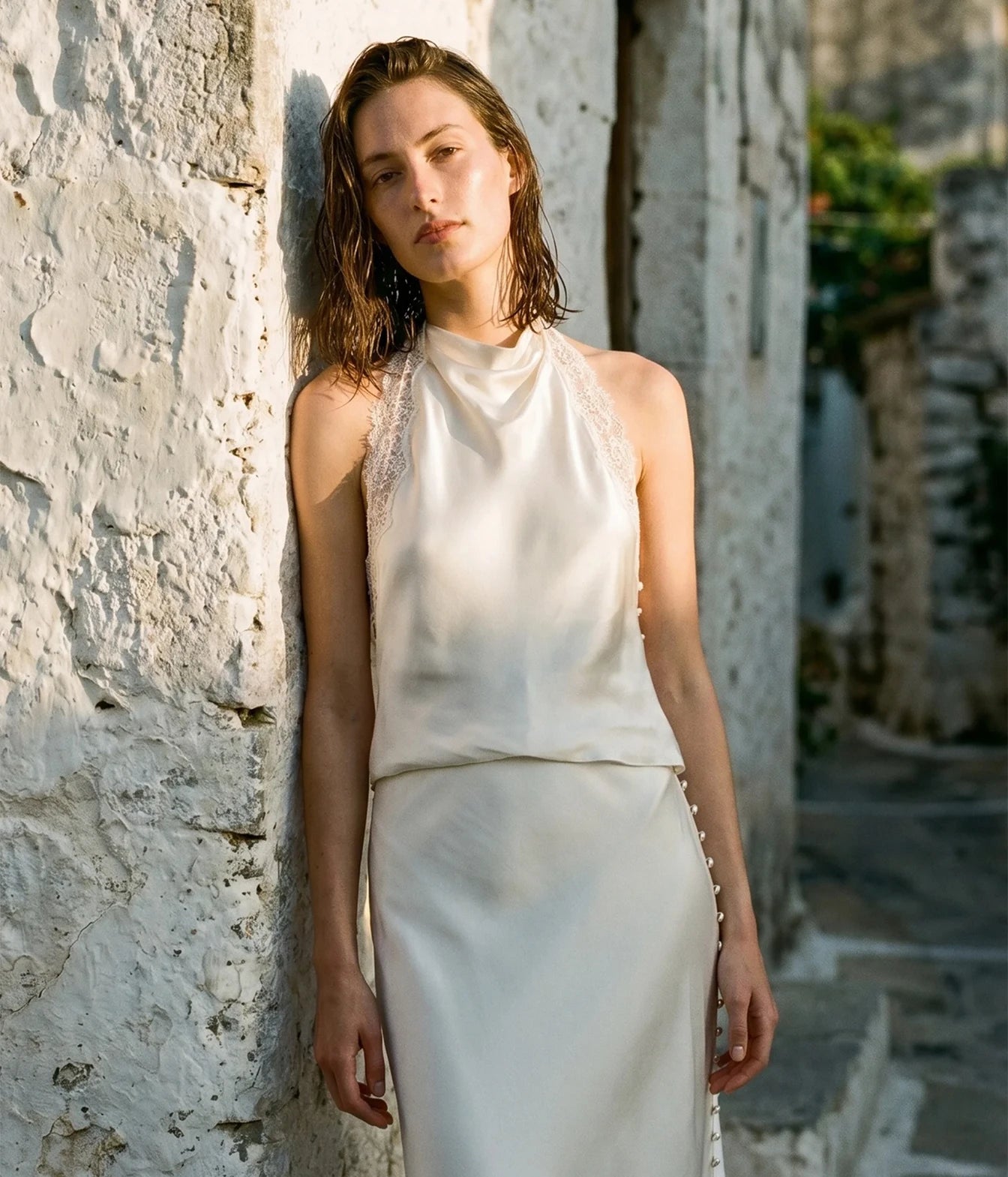 A woman wearing a sleeveless cream satin halter-neck top with lace trim