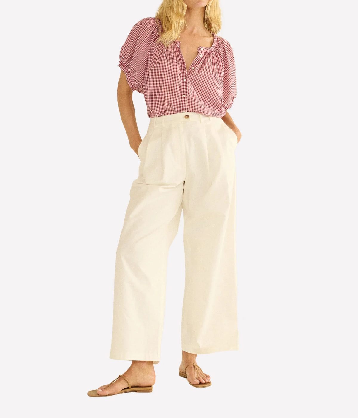 A model wearing a pink and white gingham short-sleeve blouse with puff sleeves and cream wide-leg cropped pants, paired with tan flat sandals, against a light gray background.