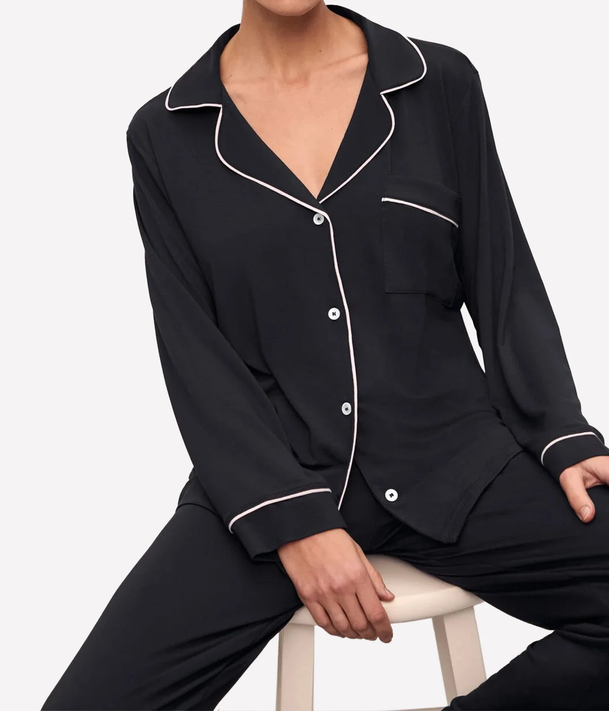 Model seated on a light wooden stool wearing the Eberjey Gisele Long Sleeve PJ Set in Black & Sorbet Pink