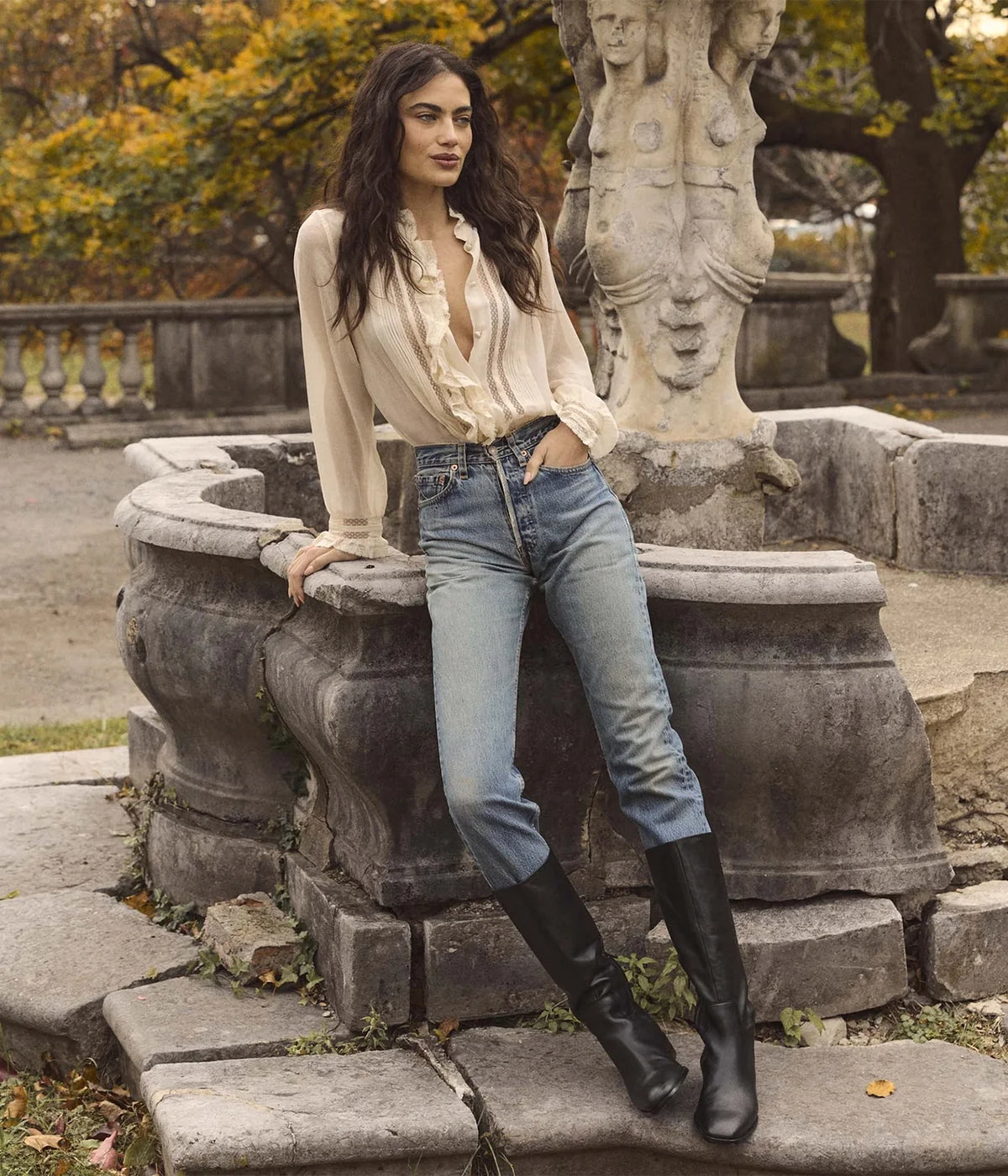 Full-length view of a model wearing the DÔEN Magdeleine Top In Candlelight tucked into light-wash jeans with black knee-high boots