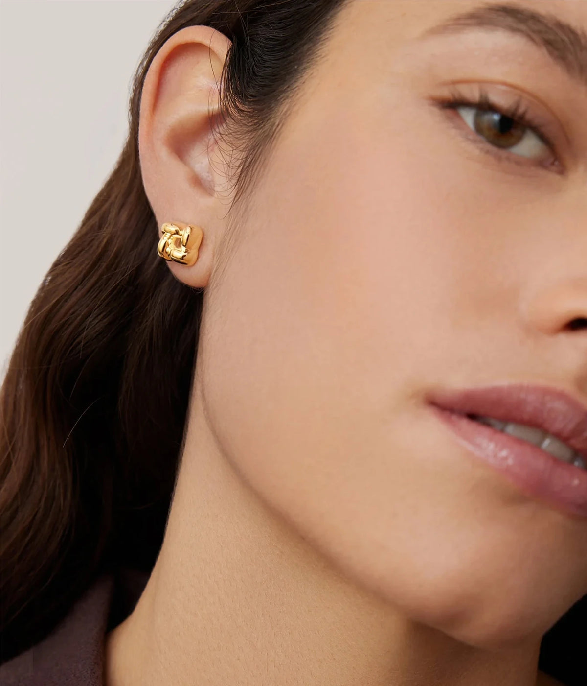 Side profile of a model with dark hair pulled back wearing the Jenny Bird Mini Woven Square Earrings in Gold with a brown top