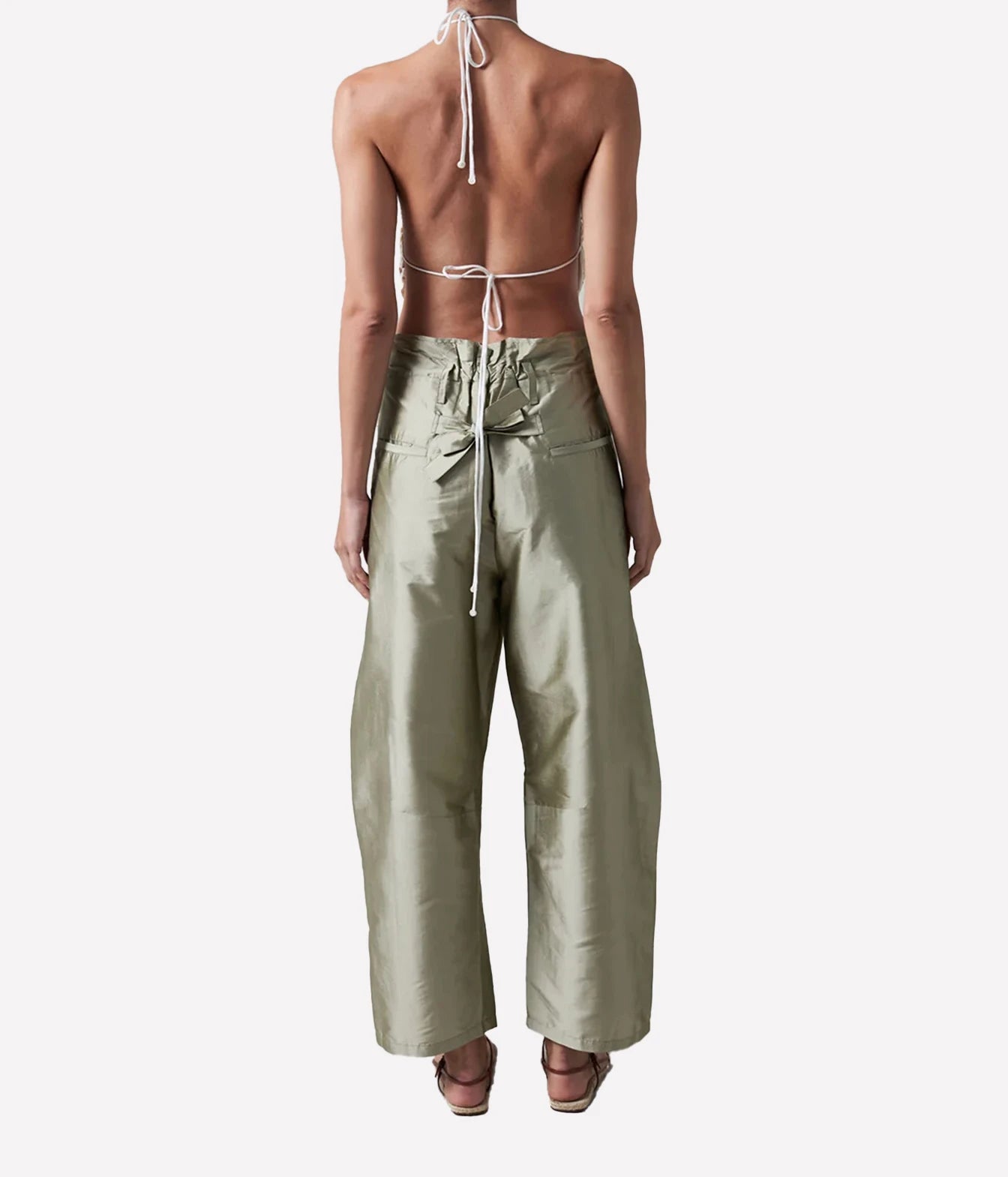 A model shown from the back wearing a light sage green halter top with a tie-back and matching wide-leg pants, set against a plain light gray background.