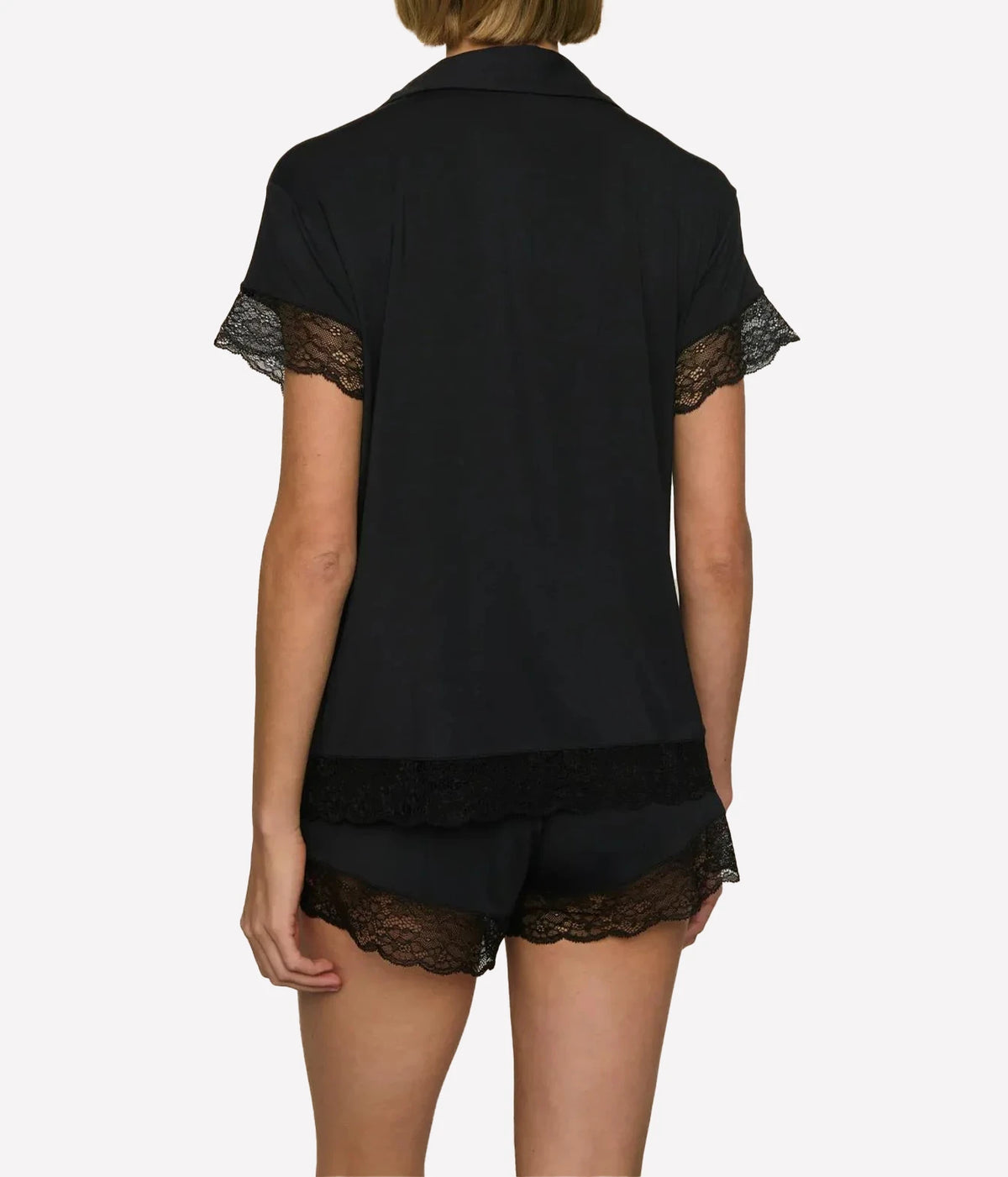 Back view of a model wearing the Eberjey Malou Lace Short Sleeve PJ Set in Black, showing the lace trim on the sleeves and along the hem of the shorts
