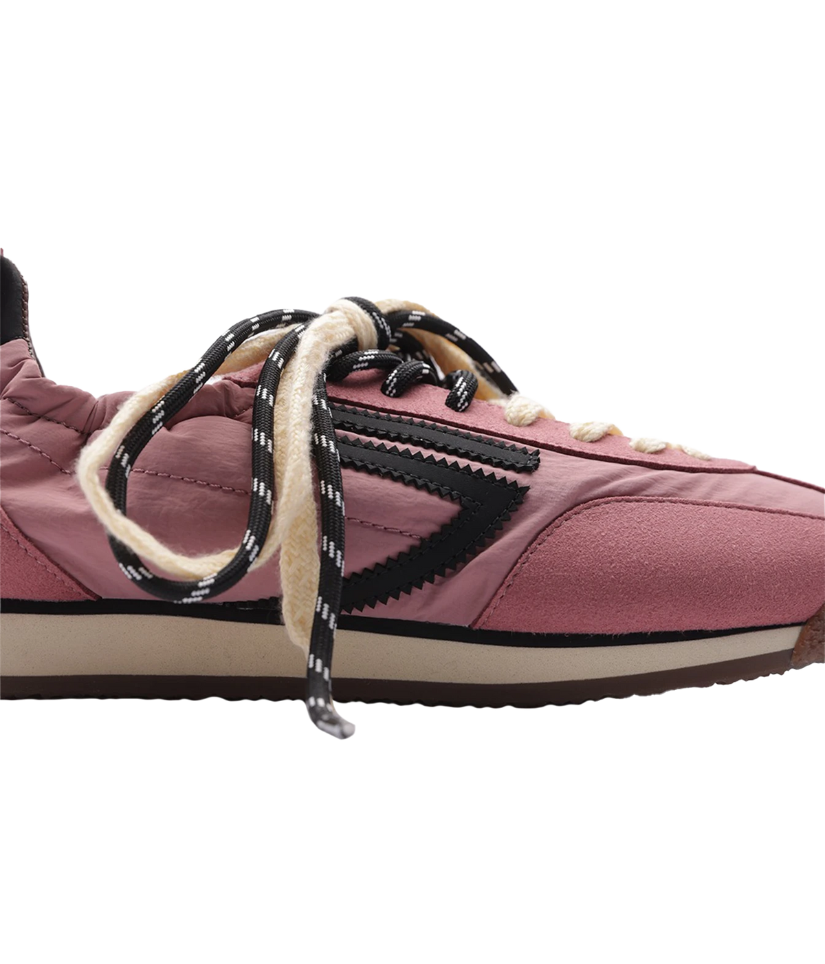 A close-up side view of a pink suede sneaker with black and white patterned laces, a black chevron side stripe, and a beige midsole on a white background.