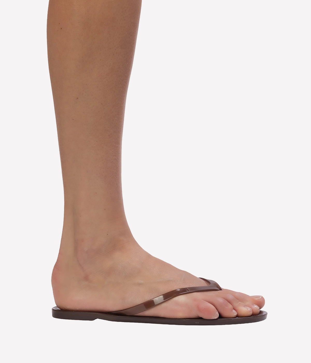 A close-up side view of a person's foot wearing a dark brown flat thong sandal