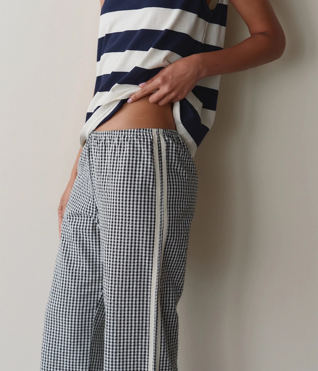 Model wearing navy gingham check pants, side view against a wall showing the waistband and side stripe detail.