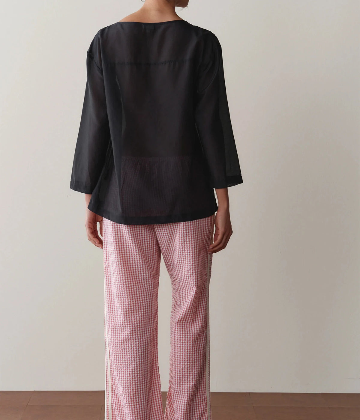 Model wearing pink gingham check pants with a black long-sleeve top, front view showing the straight-leg fit and contrast side stripe.