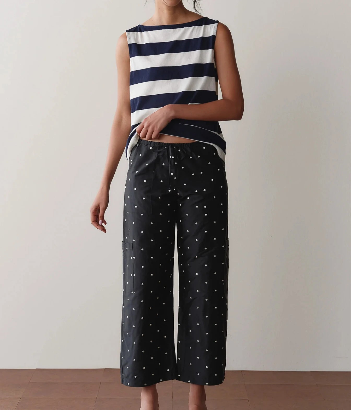 Model wearing black polka dot cargo pants with a striped tank top, standing front-on to show the relaxed straight-leg fit and drawstring waist.