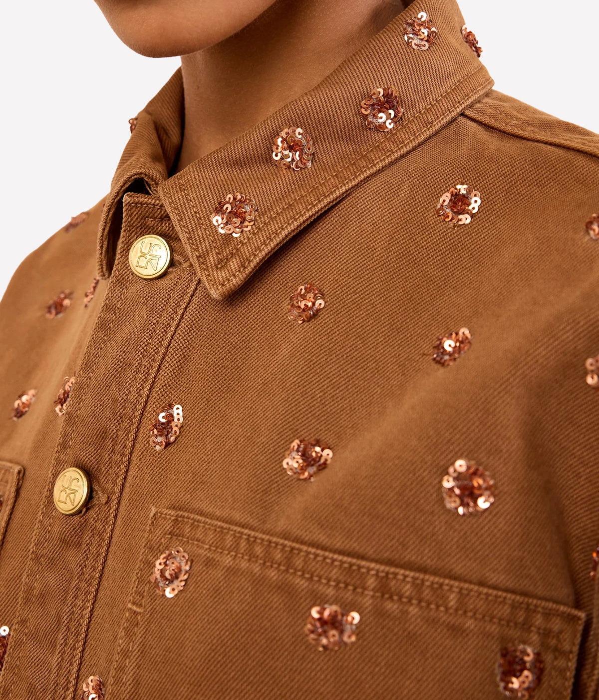 Close-up of Ulla Johnson The Bobbi Embellished Denim Jacket in Umber with floral embellishments and gold-tone buttons