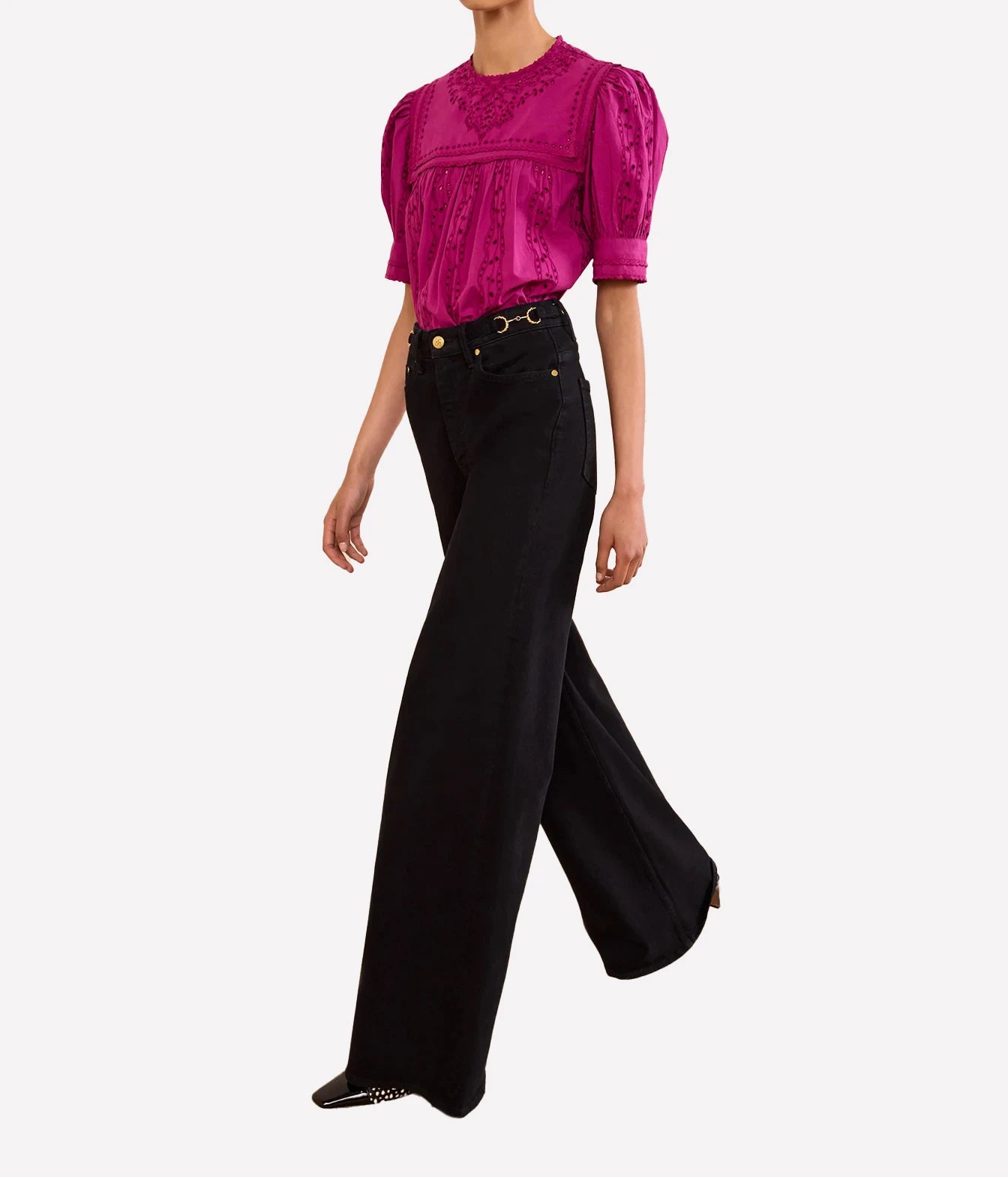 A model wearing a vibrant magenta short-sleeve blouse with puff sleeves and black wide-leg jeans, shown from the neck down against a light gray background.