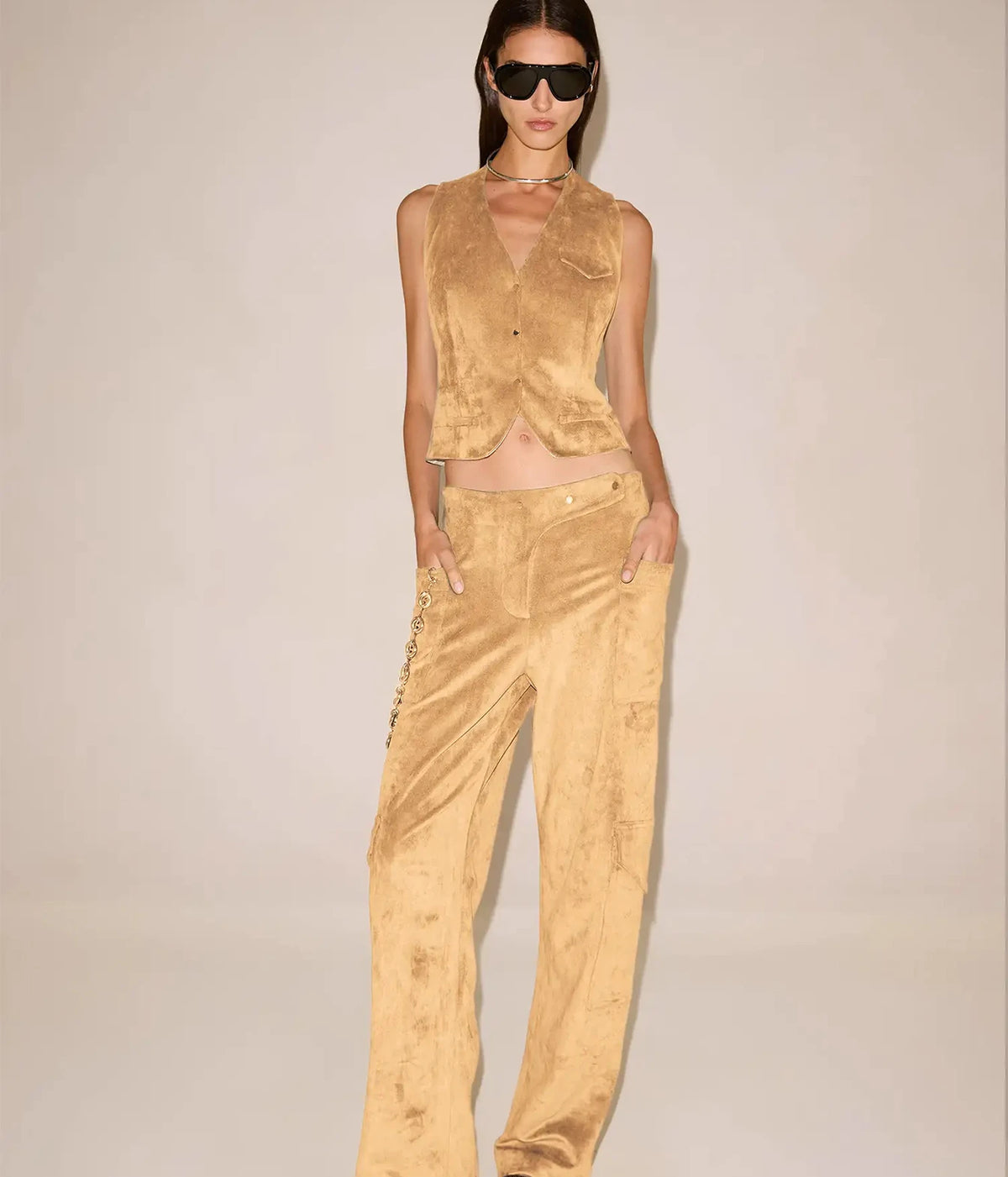 Full-length front view of a model wearing the Alexis Aquila Vest In Dune buttoned over matching wide-leg trousers with hands in pockets and black sunglasses