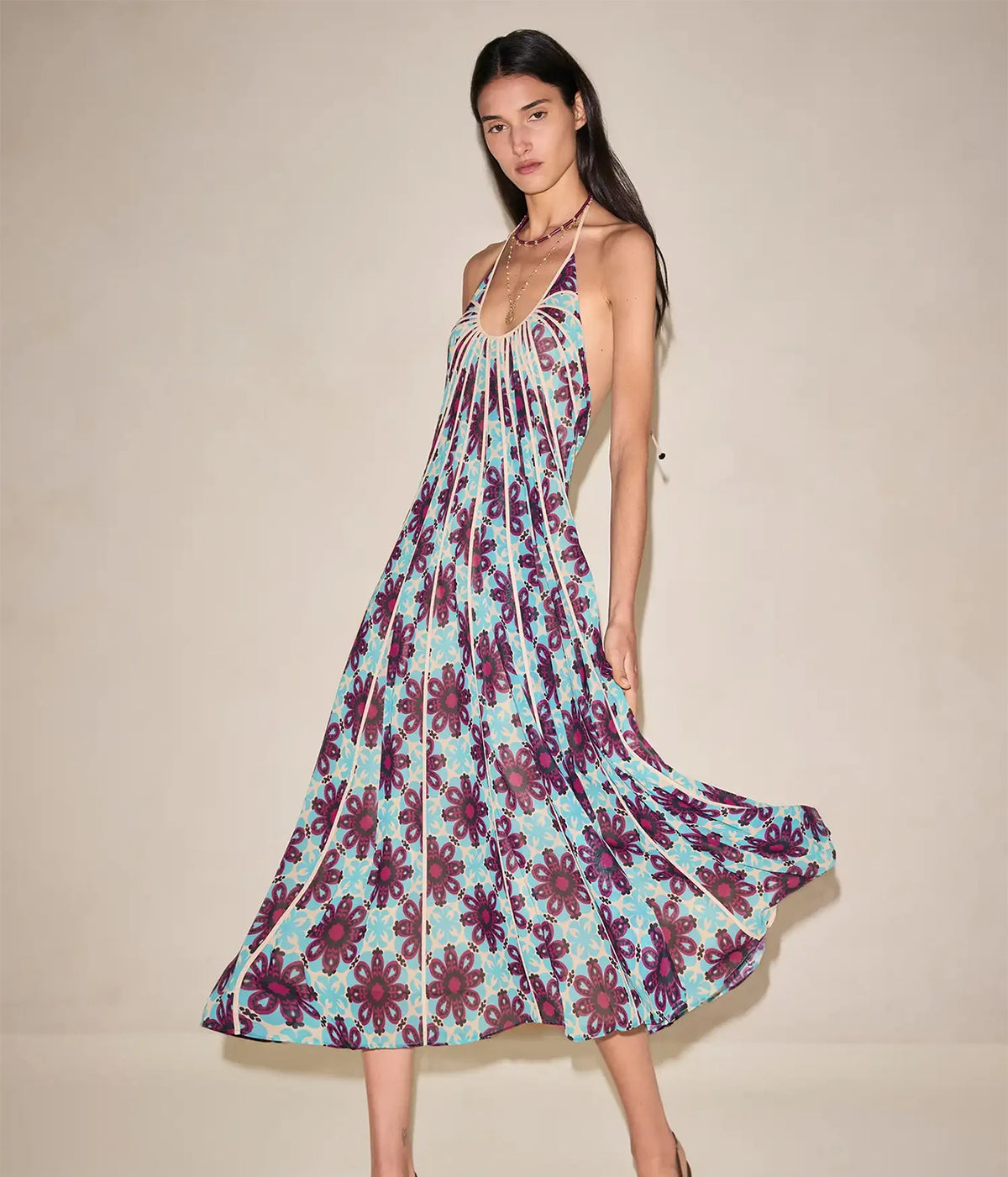 Model walking in the Alexis Azurea Dress In Jardin Sable, showing the plunging halter neckline, gathered bust and fluid midi skirt in an aqua and plum floral print swinging with movement