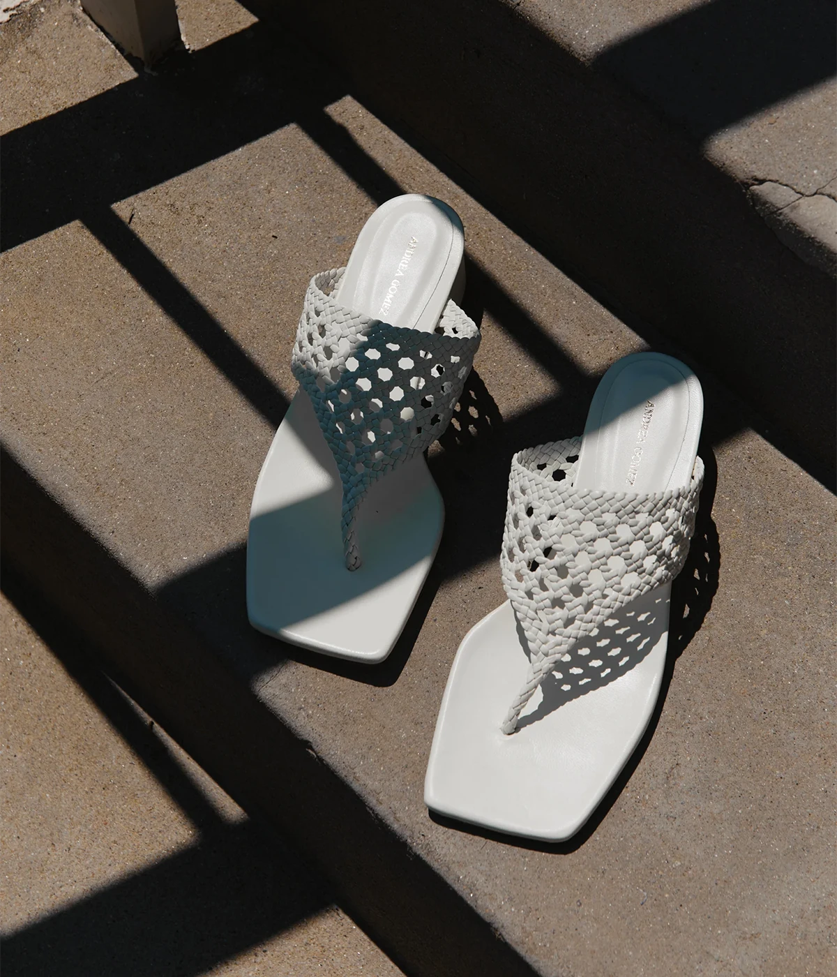White sandals with woven straps on a concrete surface