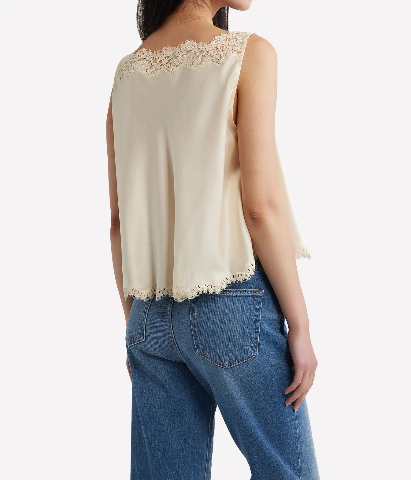 A woman shown from the back wearing a sleeveless cream top with delicate lace trim at the neckline and hem, paired with blue jeans, against a plain light background.