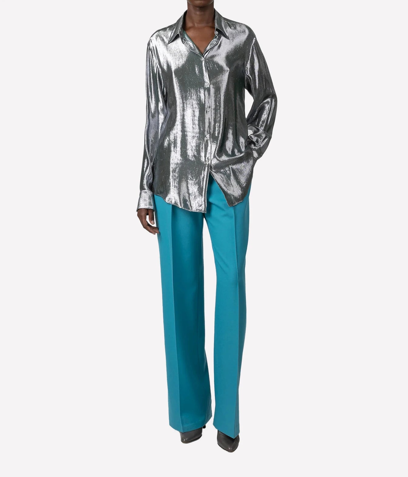 A model wearing a metallic silver satin button-down shirt and bright teal wide-leg trousers, shown from the neck down against a light gray background.