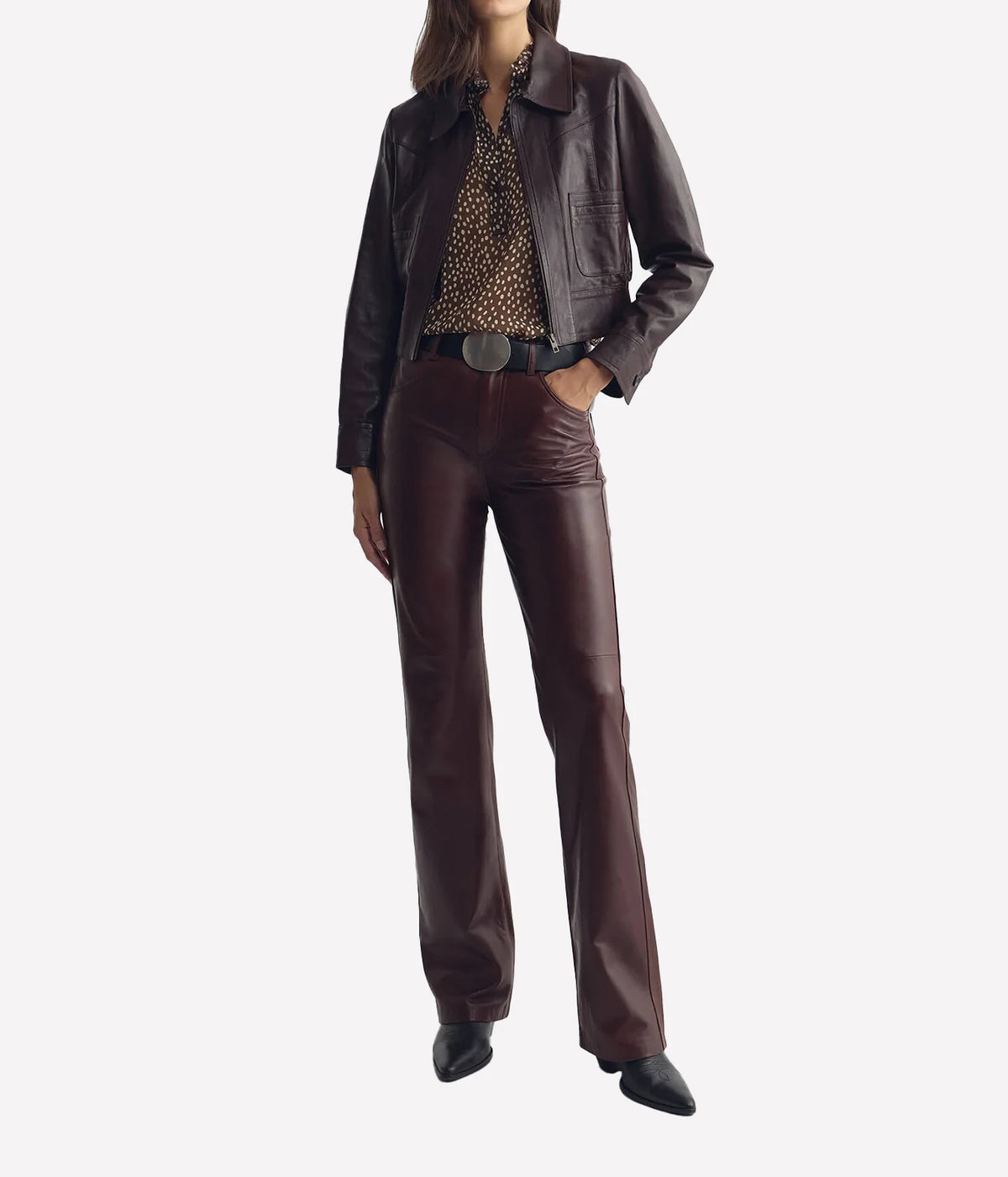 Full-length styling of a model wearing the Nili Lotan Daniella Top in Brown Cream Wild Dots layered under a Brown jacket with Burgundy trousers.