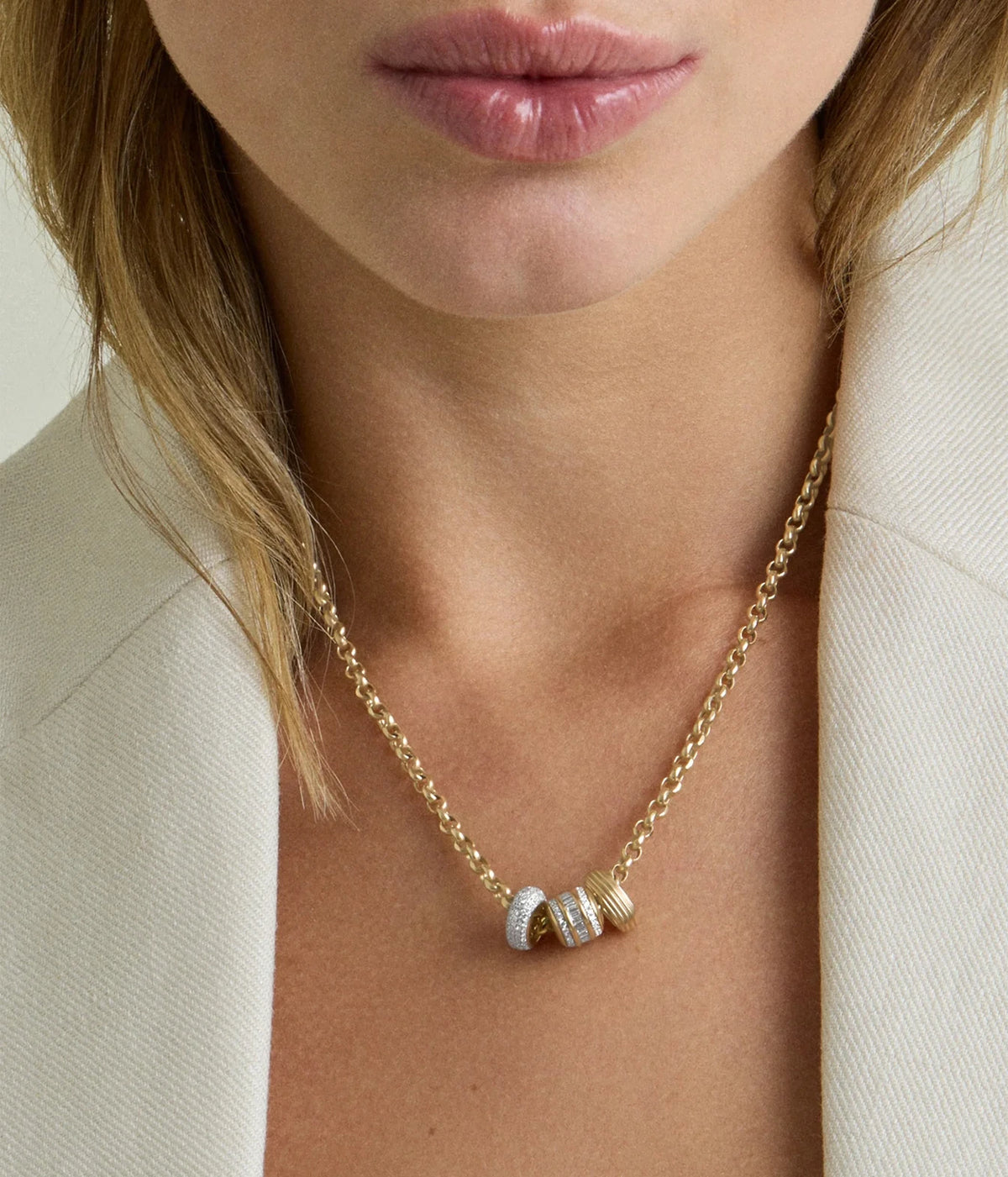 Model in a white blazer wearing the Adina Reyter Groovy Spacer Big Bead in 10K Yellow Gold alongside other beads on a gold chain