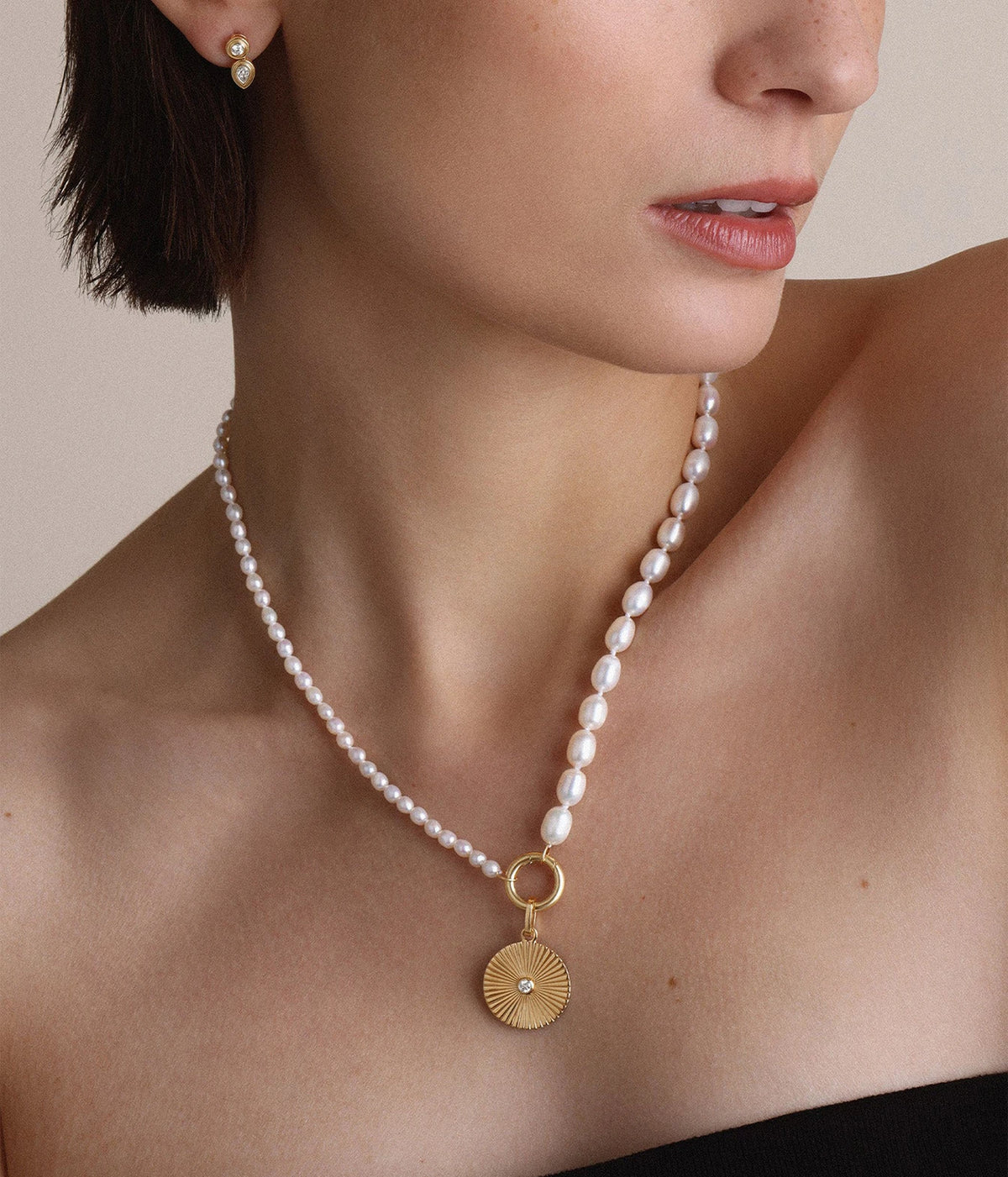 Side profile of a model in a black top wearing the Adina Reyter Half & Half Pearl Necklace in 10K Yellow Gold with a gold coin pendant on the clasp
