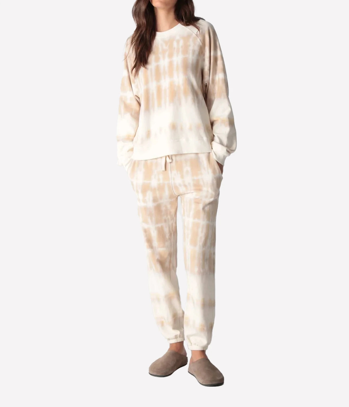 Full-length front view of a model wearing the Electric Rose Classic Horizon Jogger in Dune Ivory with a matching tie-dye crew-neck sweatshirt, hands in pockets and taupe suede clogs