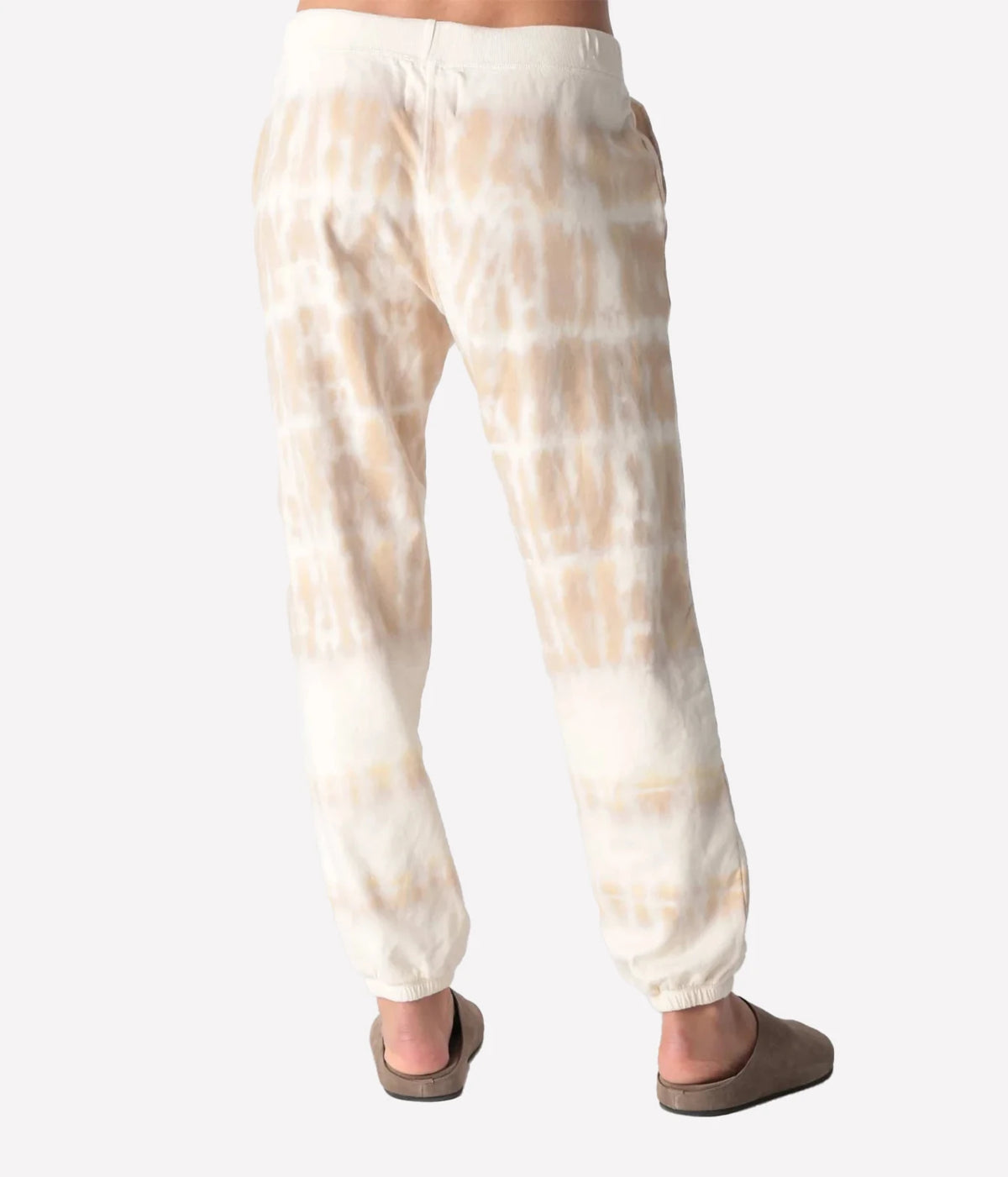 Back view of a model wearing the Electric Rose Classic Horizon Jogger in Dune Ivory, showing the relaxed fit and the tie-dye fading towards the cuffed hem, with taupe suede clogs