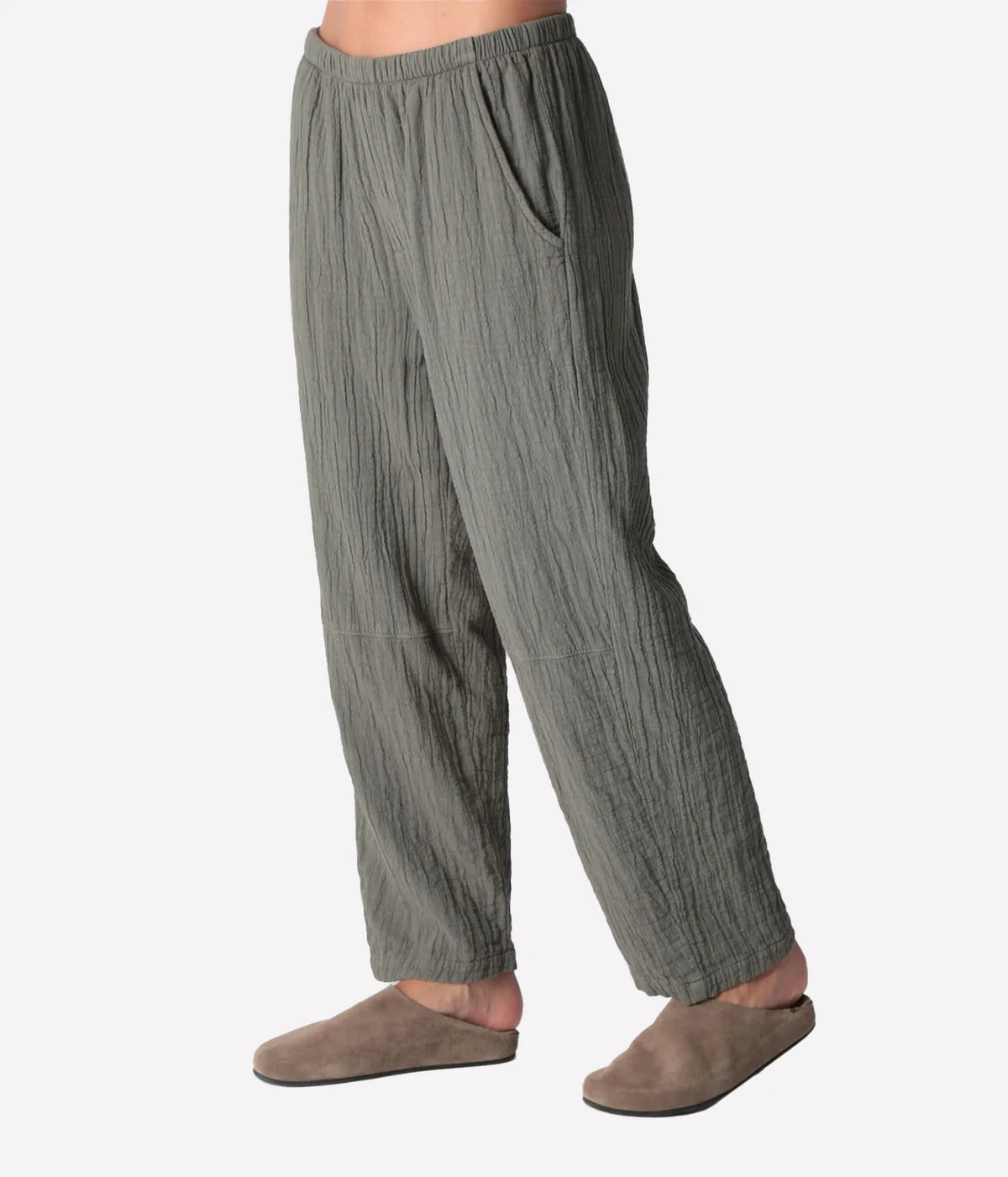 Side profile of a model wearing the Electric Rose Kick Back Pant in Moss, showing the slanted side pocket, knee seam, with taupe suede clogs