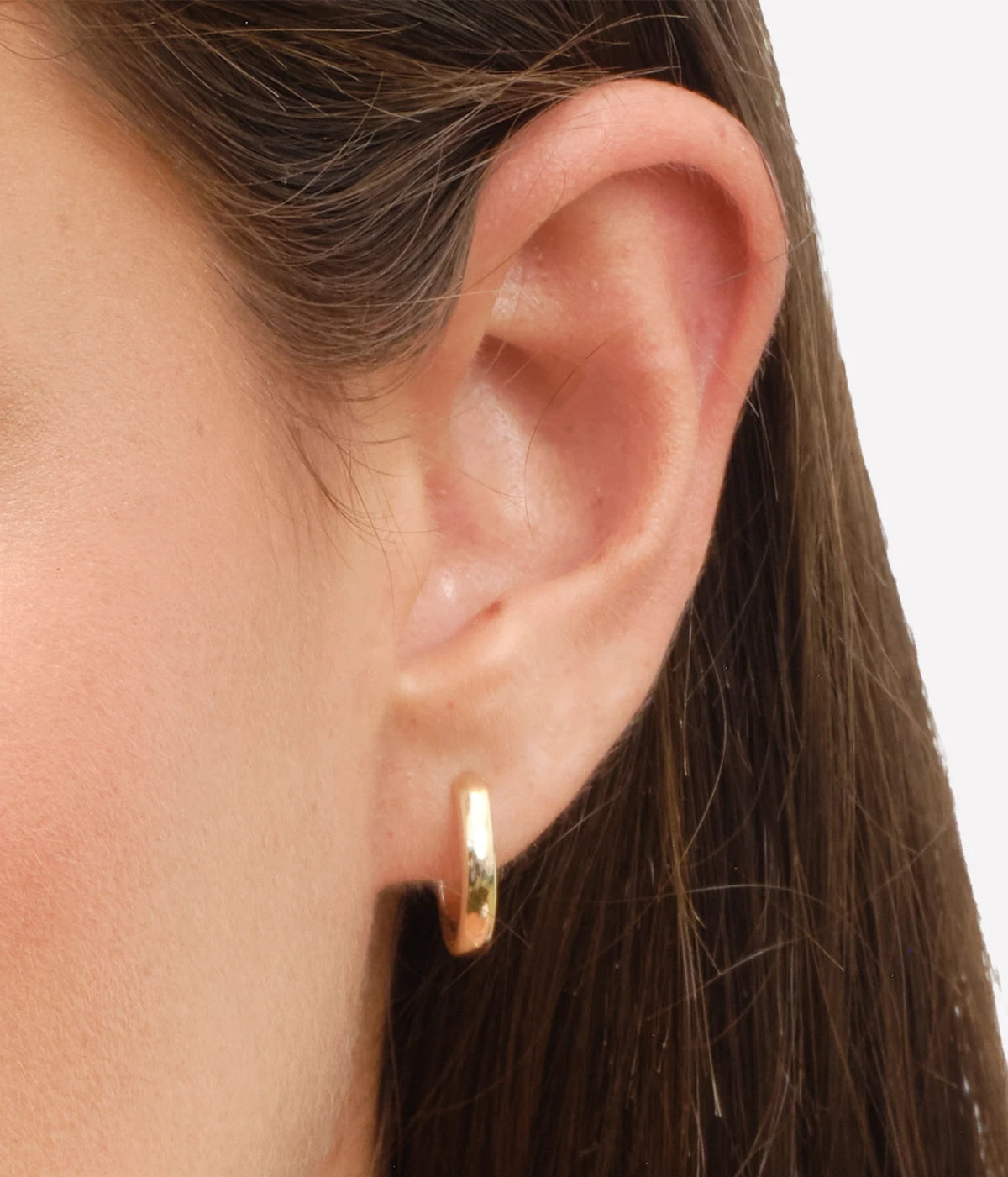 Close-up of a model wearing the LANA Gold Hinged Huggies in Yellow Gold in her ear, showing the small huggie sitting snugly on the lobe