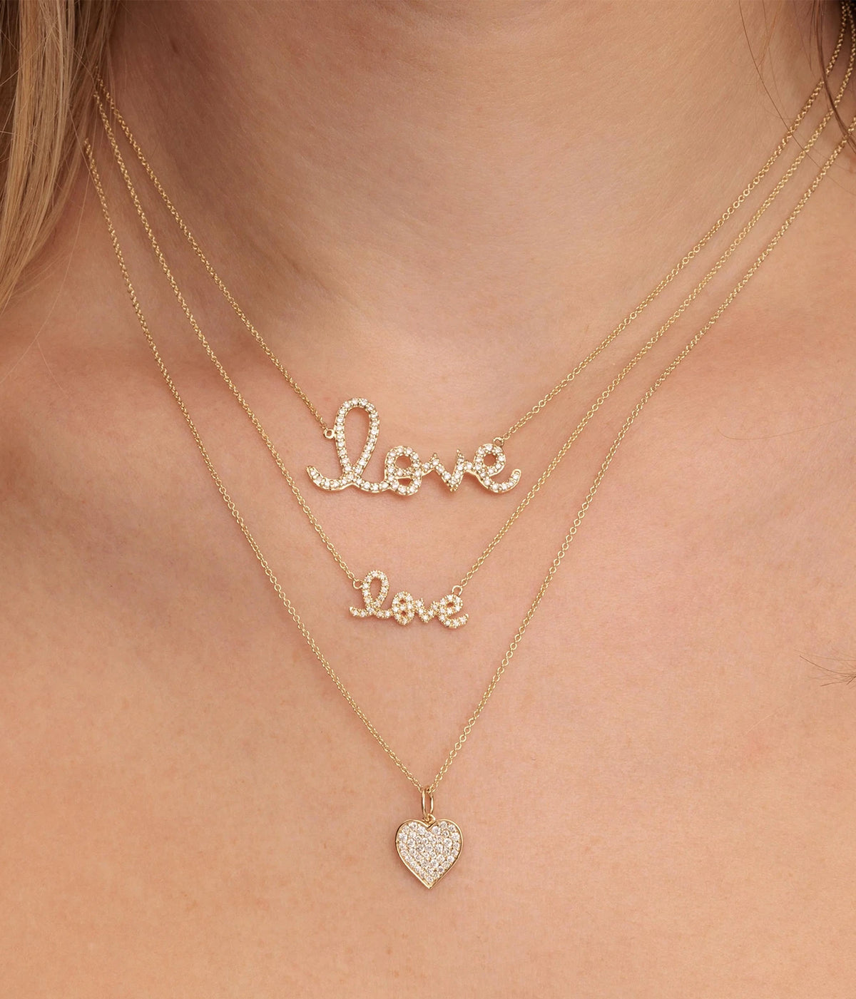 Model wearing the Sydney Evan Love Script Necklace In 14K Yellow Gold layered with a smaller "Love" necklace and a diamond heart pendant on fine gold chains