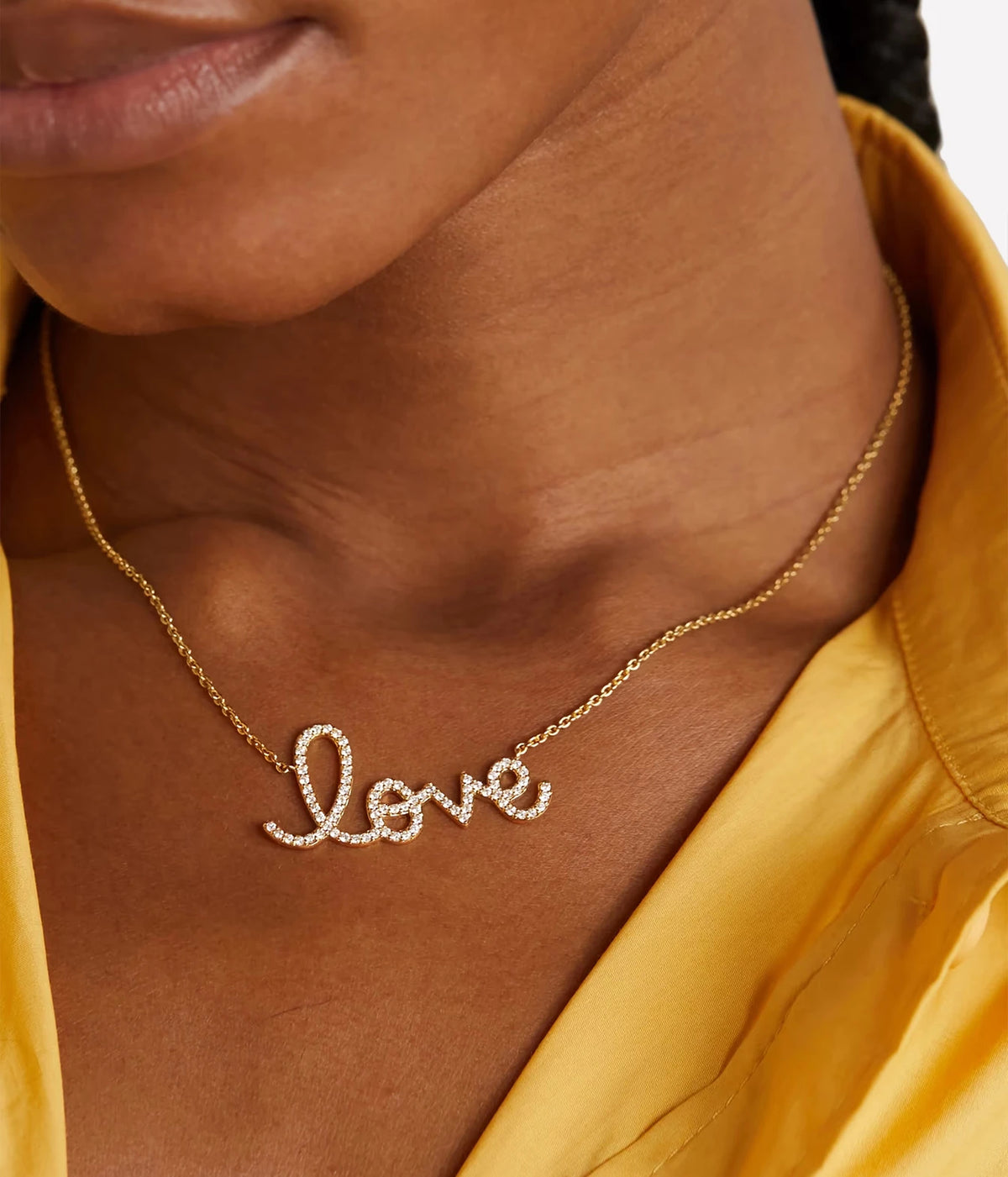 Model wearing the Sydney Evan Love Script Necklace In 14K Yellow Gold at the collarbone with a golden yellow collared top