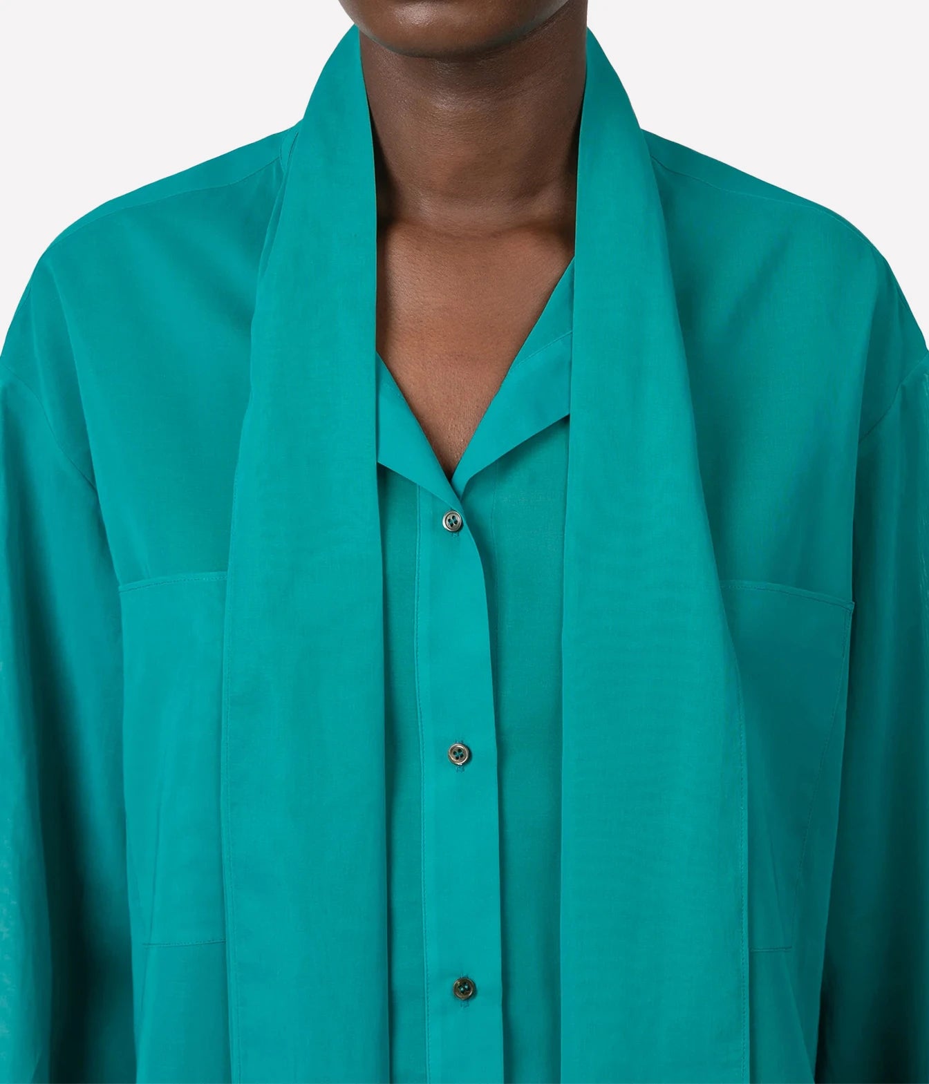 A close-up of a model wearing a vibrant teal green button-down shirt with a draped collar, set against a plain light gray background.