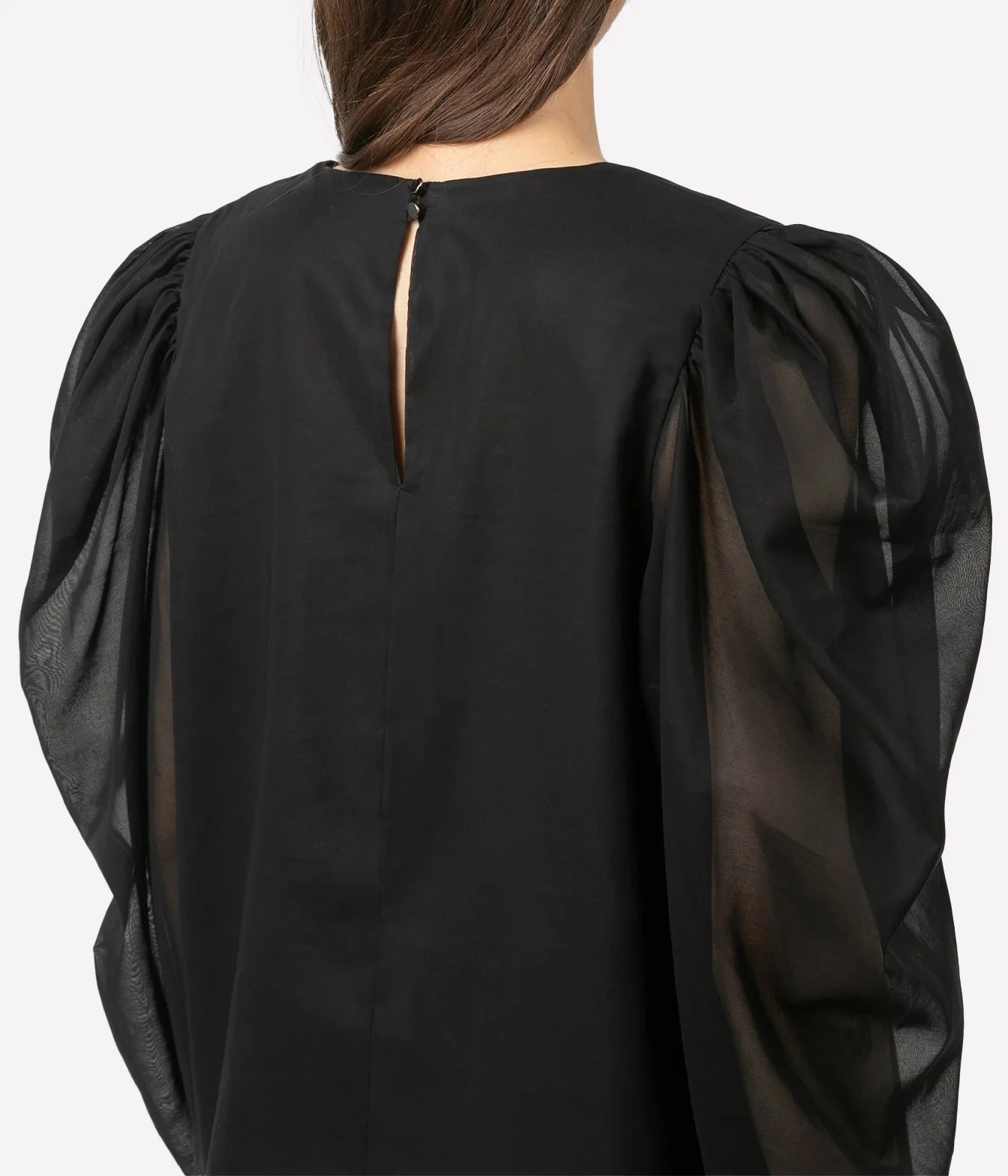Back view of a black blouse with dramatic sheer puff sleeves and a small keyhole back detail, shown on a model against a light gray studio background.